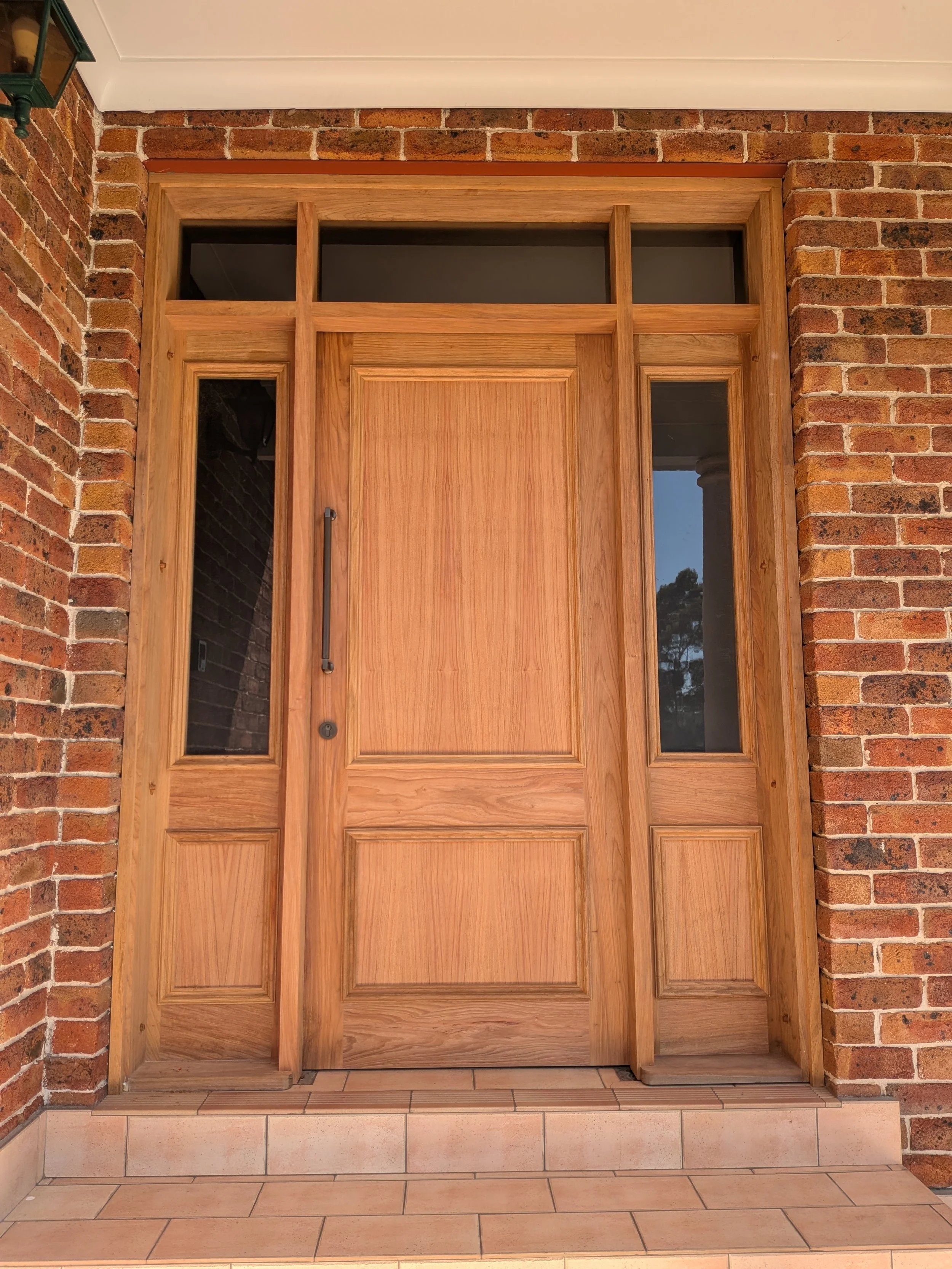 Wooden front door set in red brick exterior wall, with remaining bricks above and around the door frame and white trim at top.