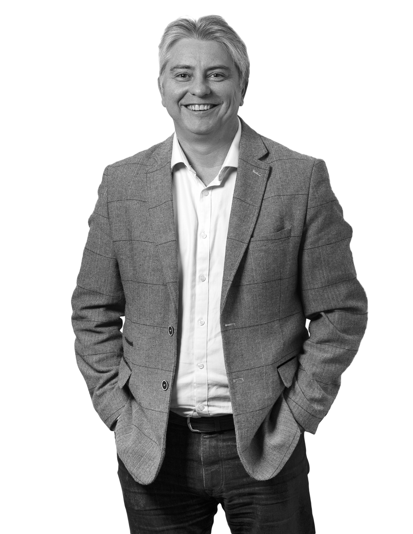 A black and white photograph of Andrew Allen wearing a blazer over a collared shirt, standing with hands in his pockets against a plain background.