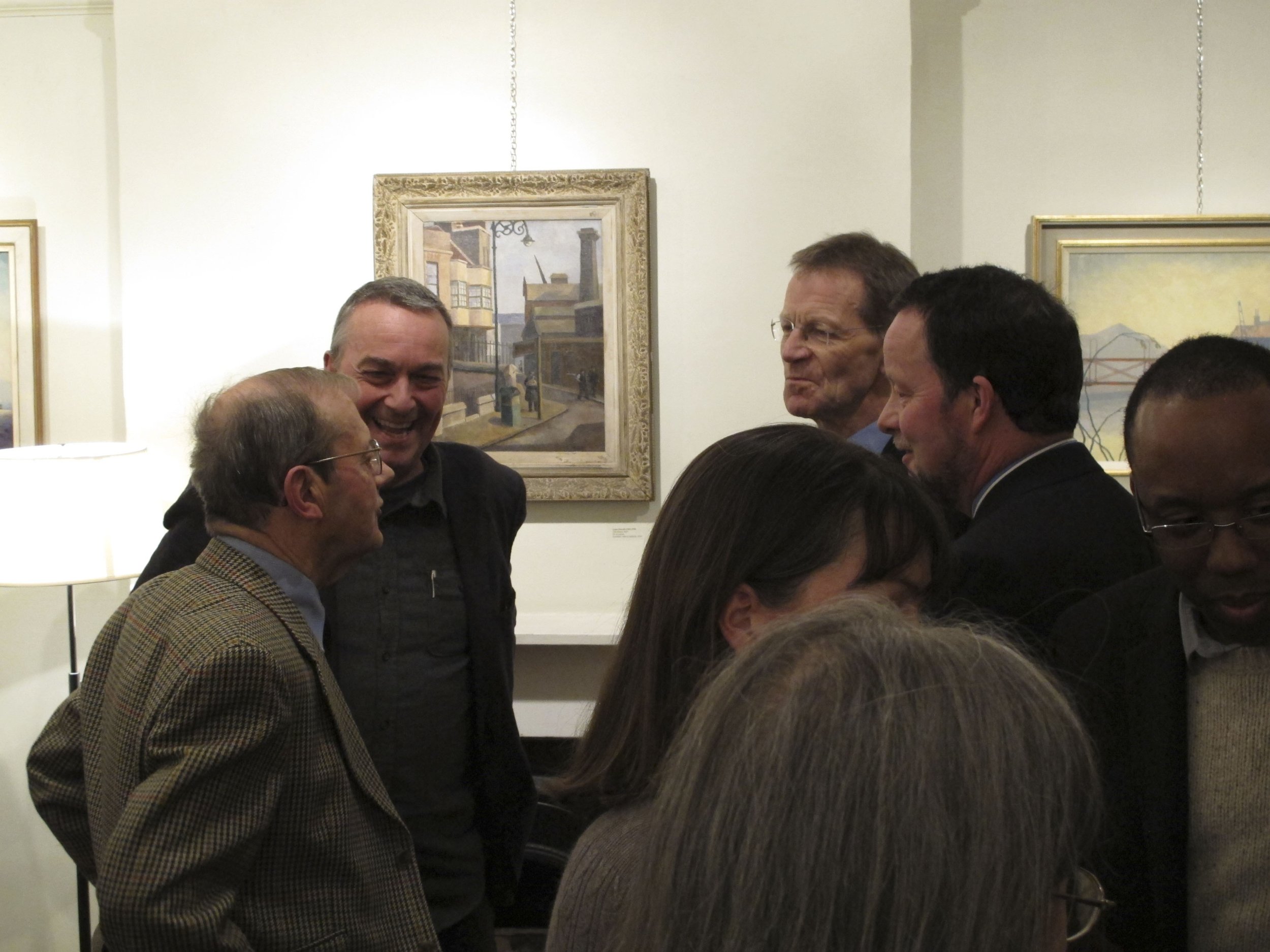 Group of people engaged in conversation at an art gallery, with paintings on the wall behind them.