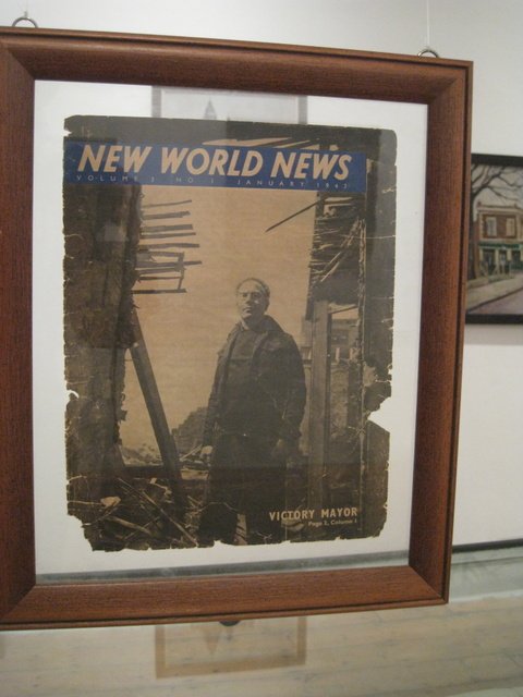 Framed front page of an old newspaper titled 'New World News' showing a man standing amid the ruins of a destroyed building.