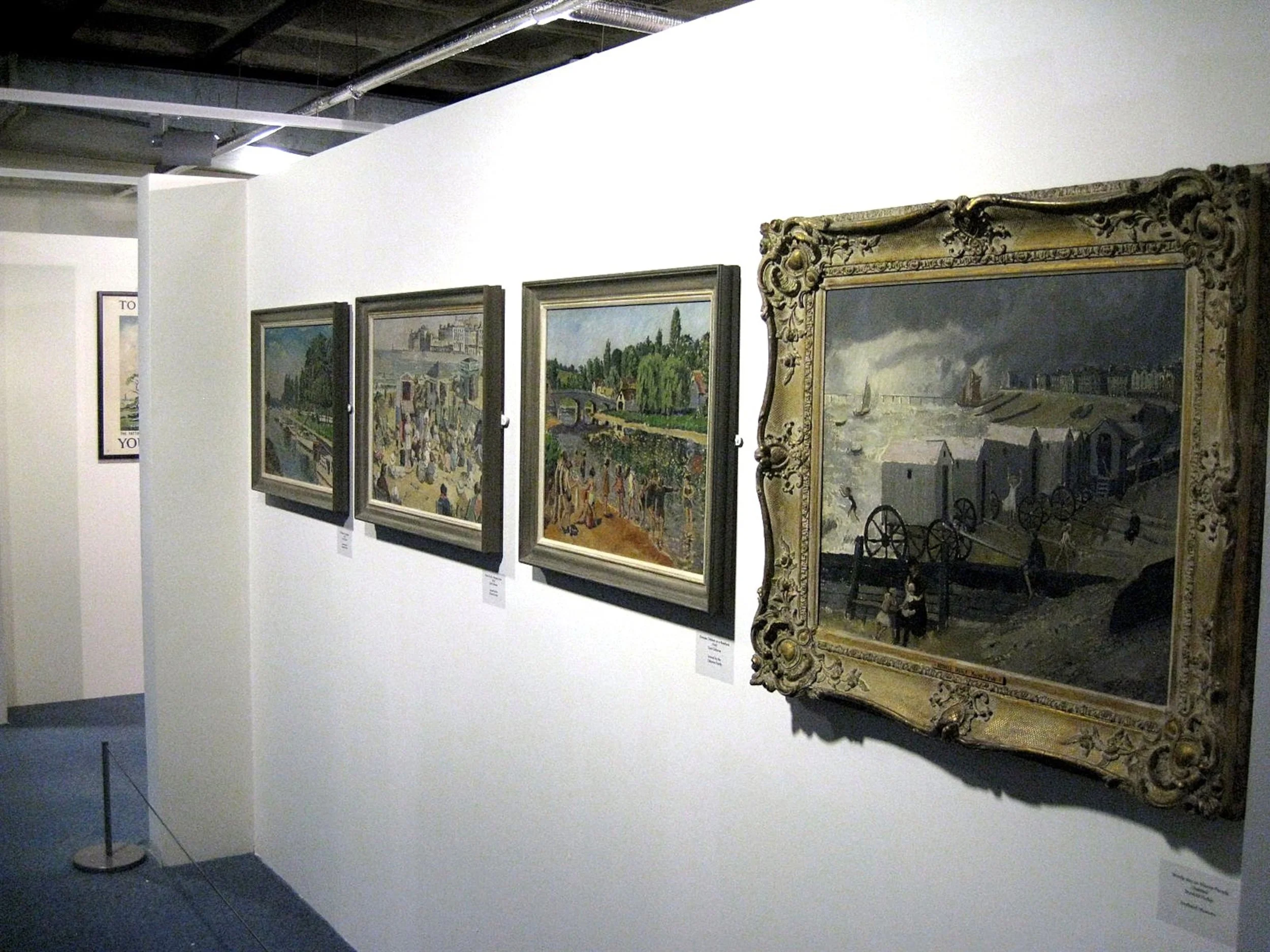A gallery wall displaying five framed paintings, with the rightmost featuring a harbor scene with boats, a bridge, and dark clouds in the sky.