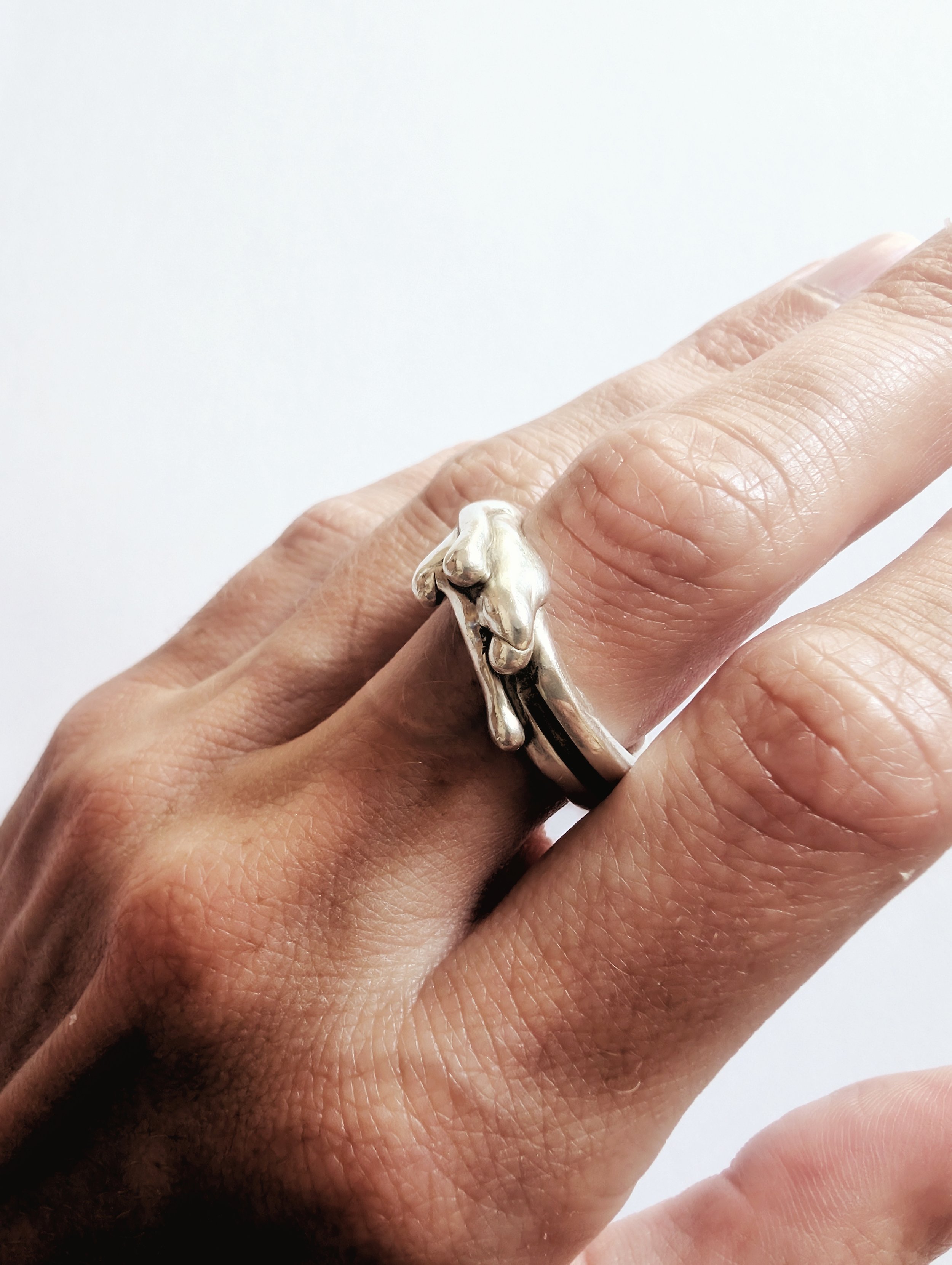 Hand wearing a silver ring with a sculpted organic form wrapped over the band