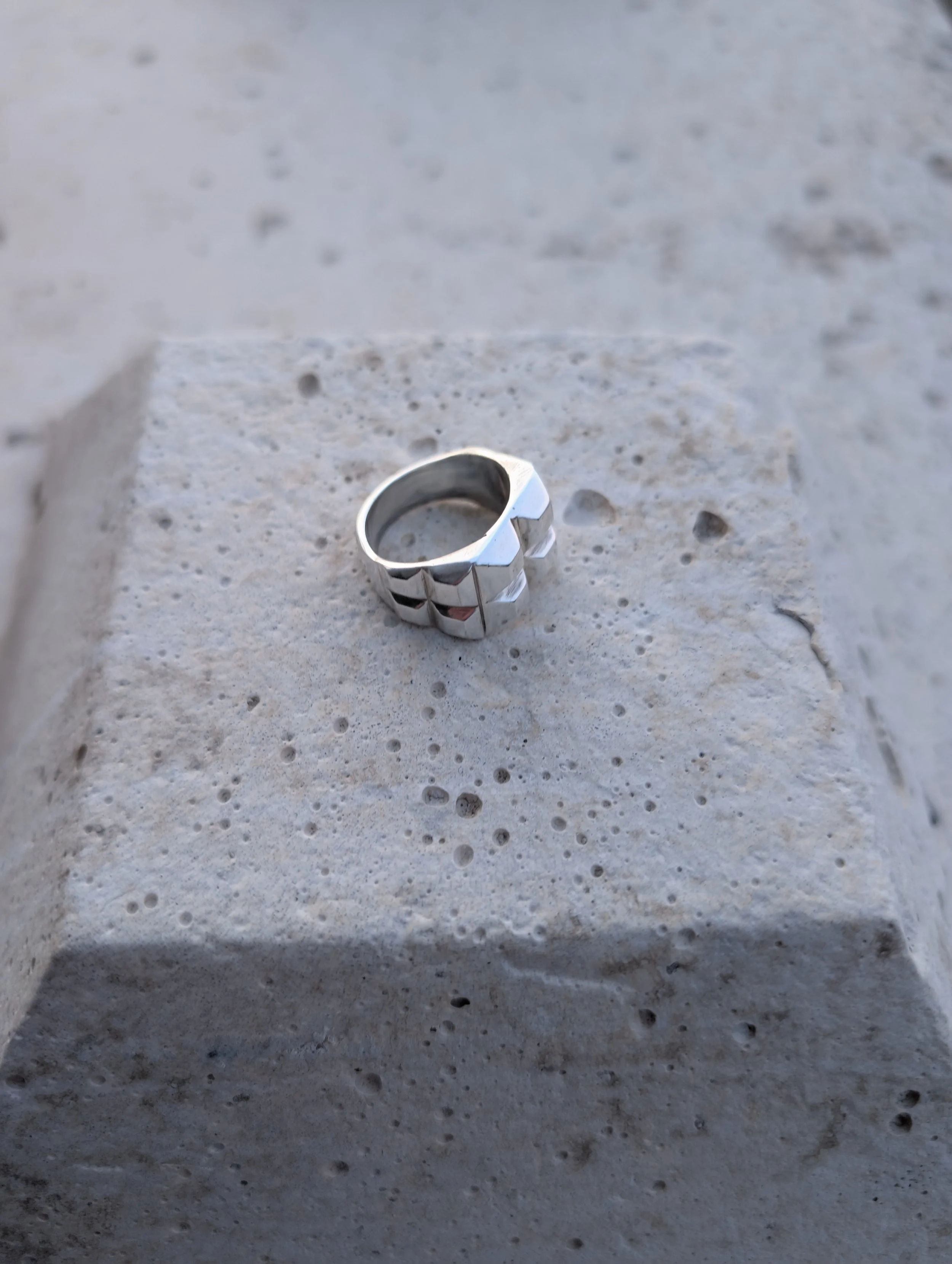 Polished sterling silver ring with a faceted, stepped top on a concrete block