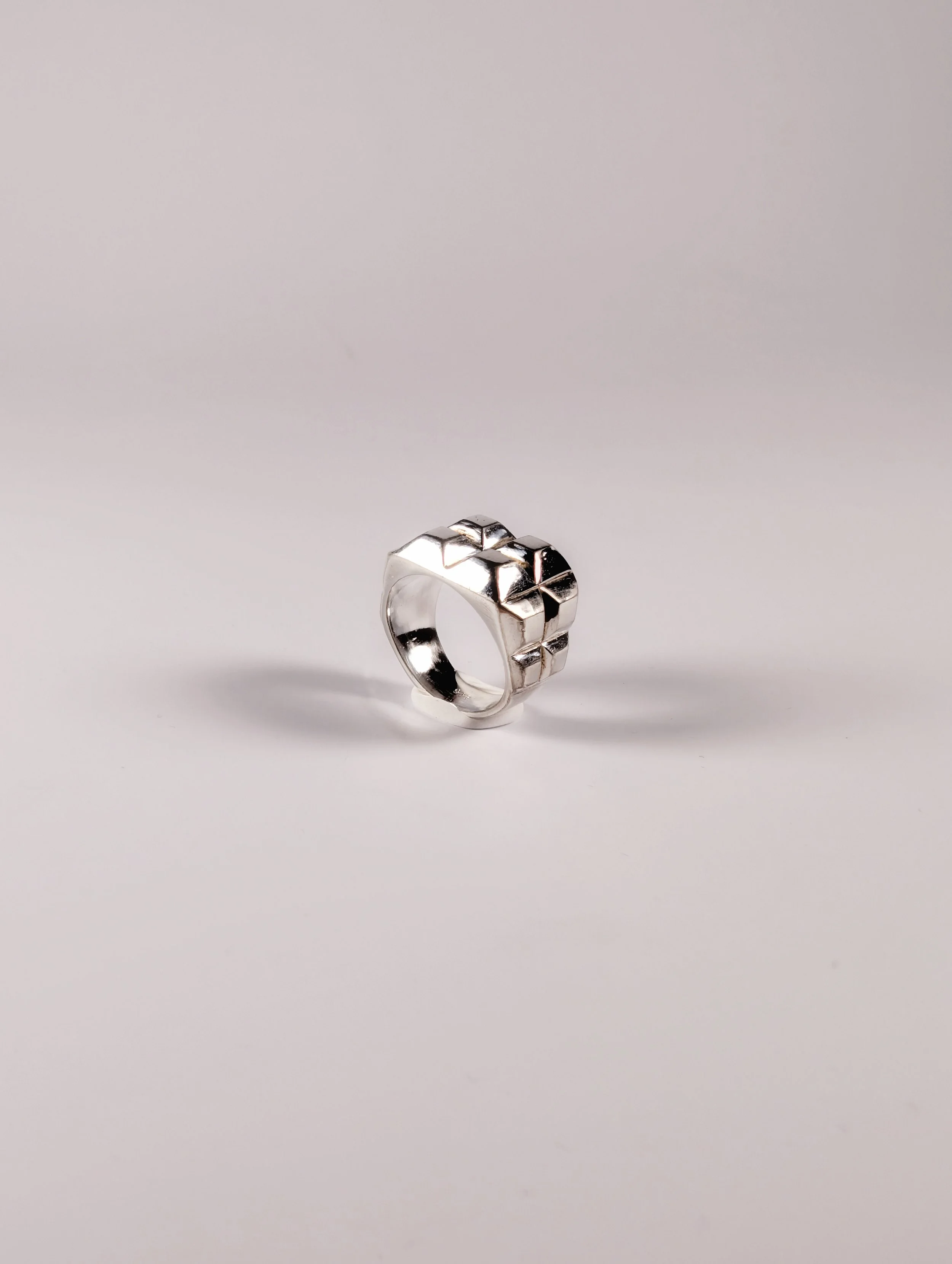 Polished silver ring with a raised geometric block pattern, three-quarter view