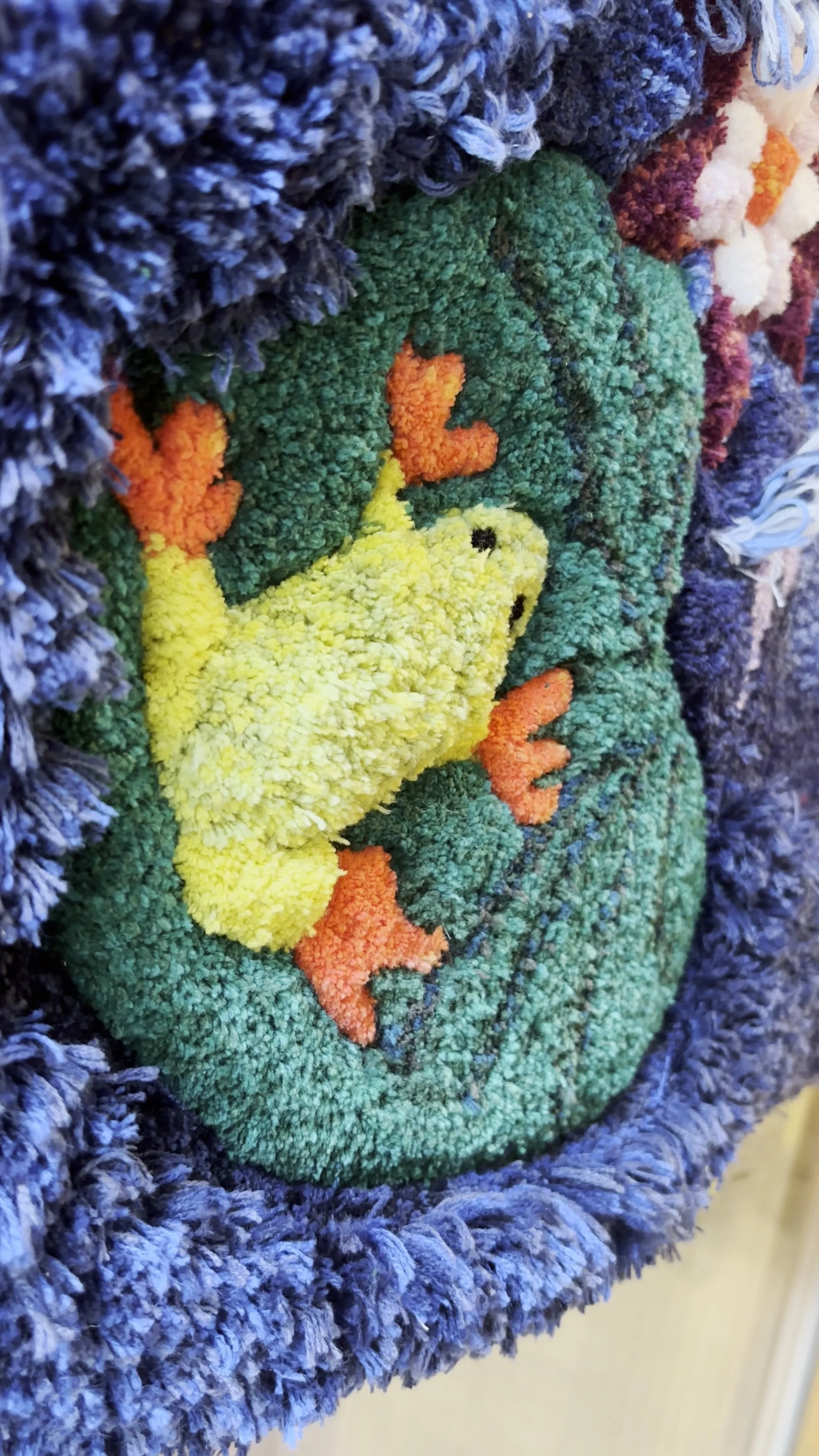 A textural rug of a 3D frog resting on a lily pad