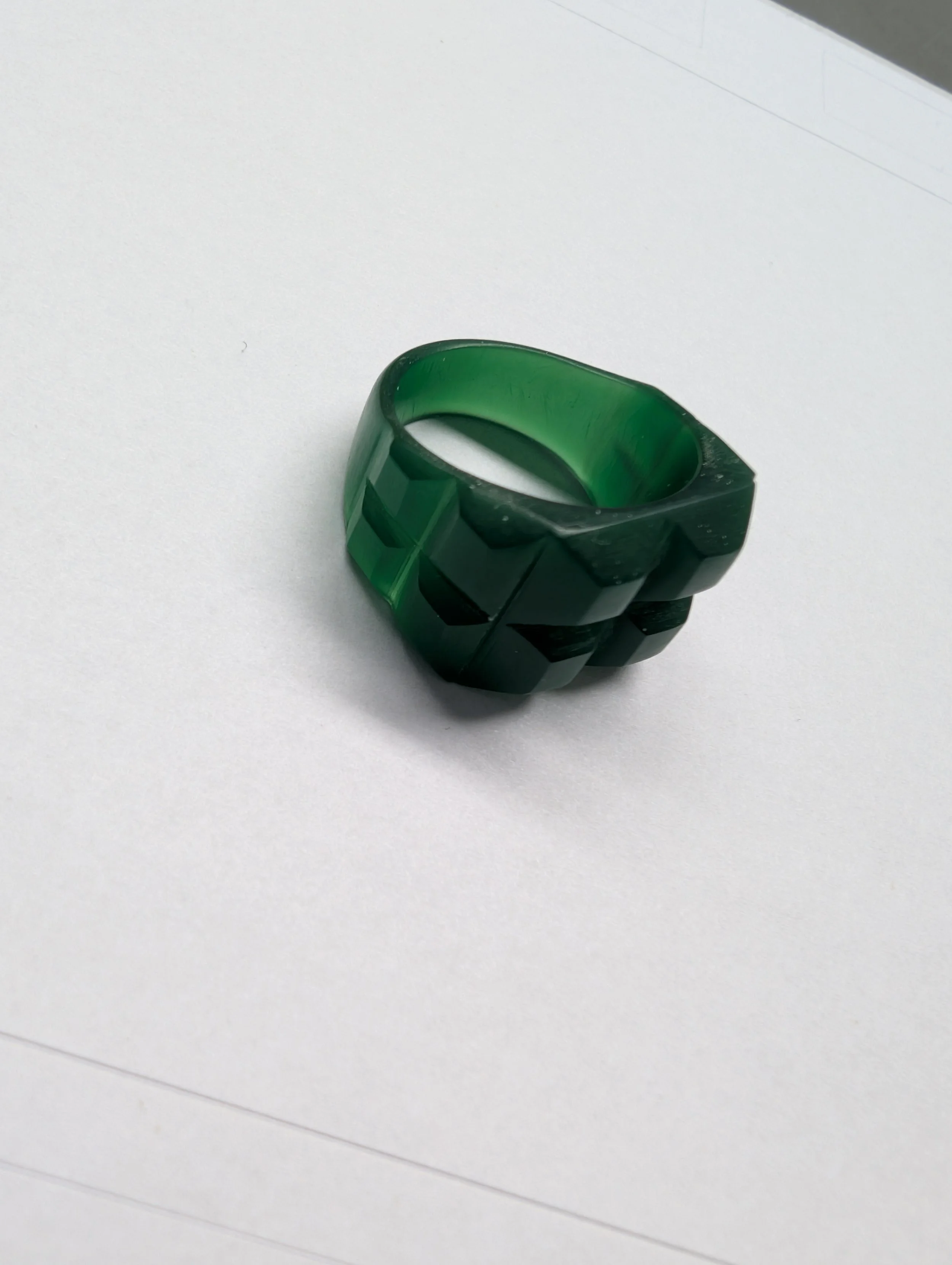 Finished green wax ring model with a faceted, stepped top on white paper. Created at a workshop at Tuft Tuft by Alexandre Nicolet