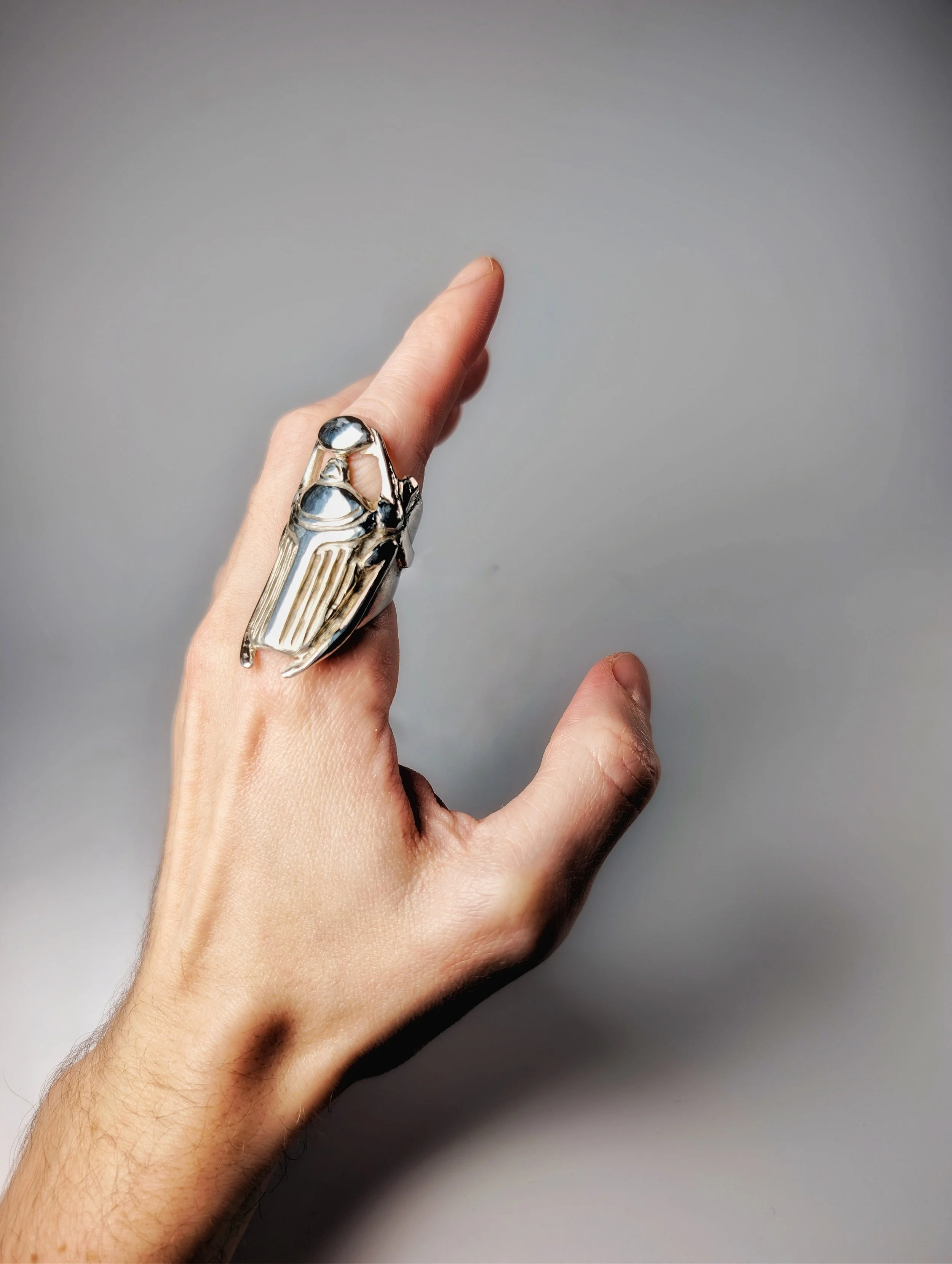 Hand wearing a long silver scarab beetle ring across the finger