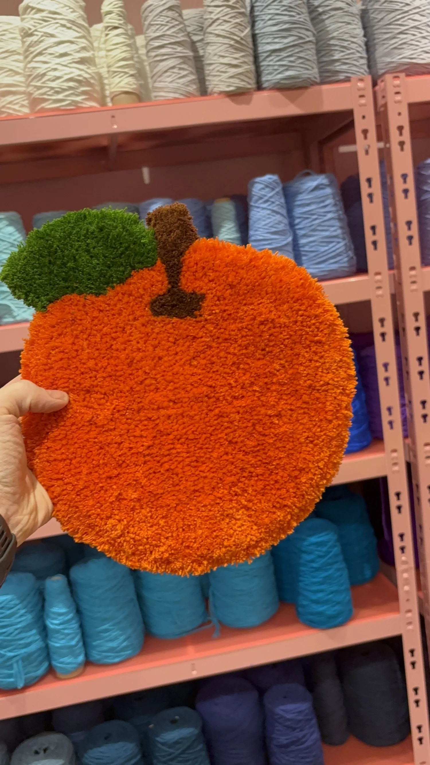 Kleiner Teppich in Form einer Orange, vor der Garnwand hochgehalten
