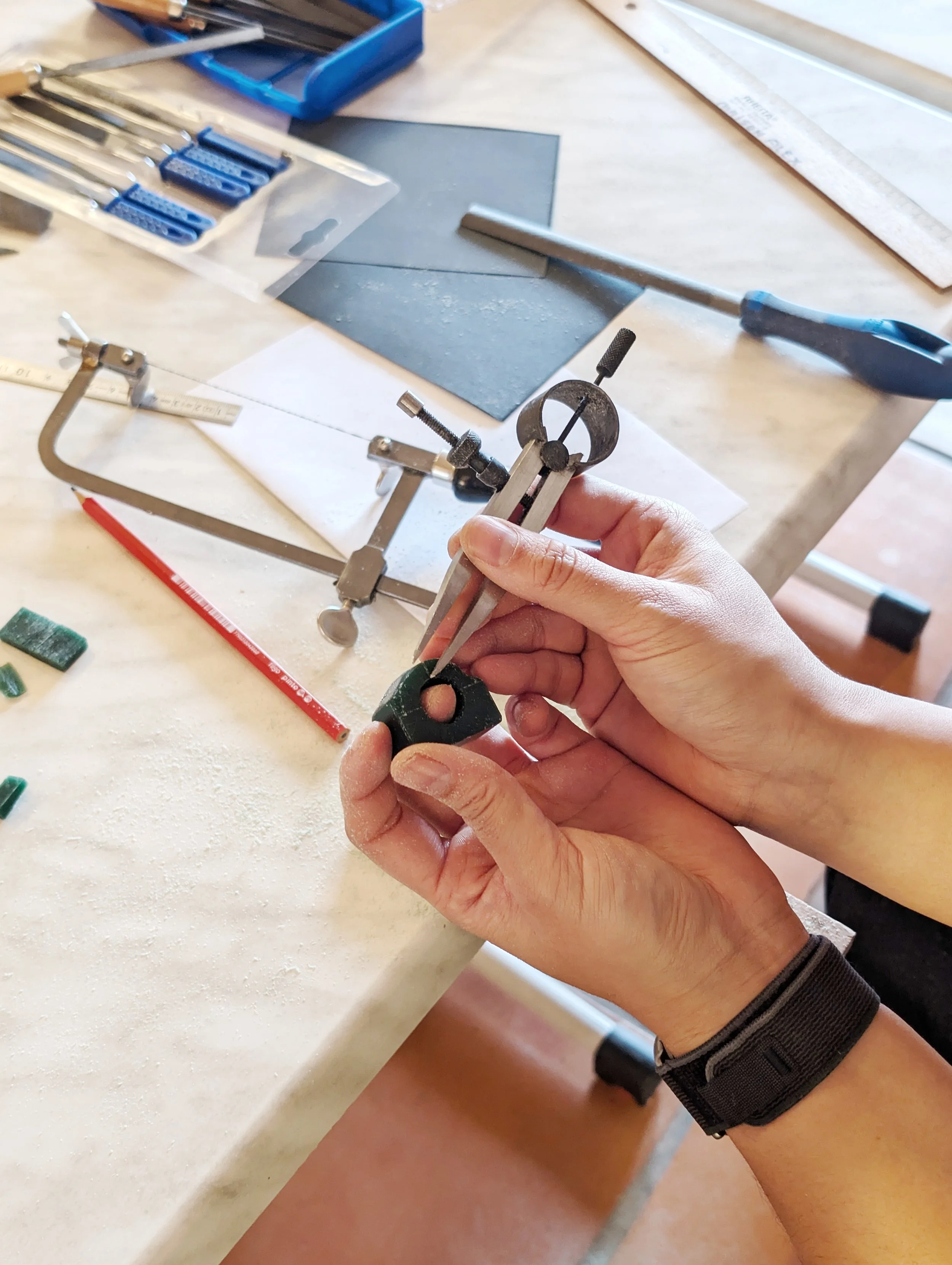 Participant measuring a small green wax ring block with dividers at a jewellery workbench