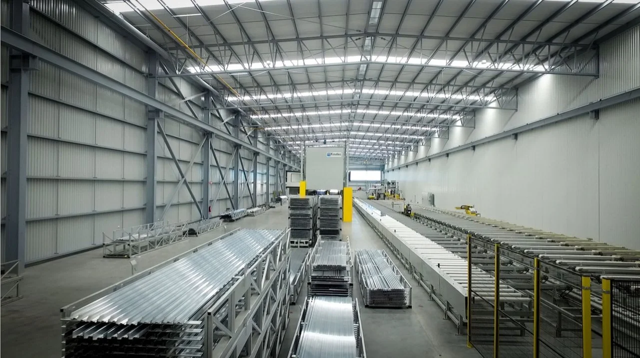 Interior de una planta industrial moderna con estructuras metálicas y tuberías organizadas en un amplio espacio con techo alto.