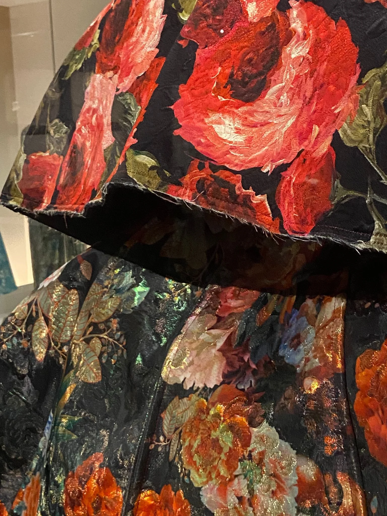 Veste ou robe en tissu brodé avec un motif floral de roses rouges, roses pâles, et feuillagess dorés et verts sur fond noir.