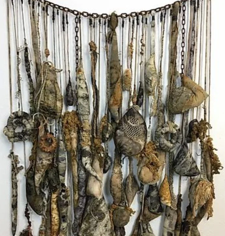 Une installation artistique composée de dizaines de morceaux de tissus ou de matériaux suspendus à des chaînes, formant un mur décoratif.