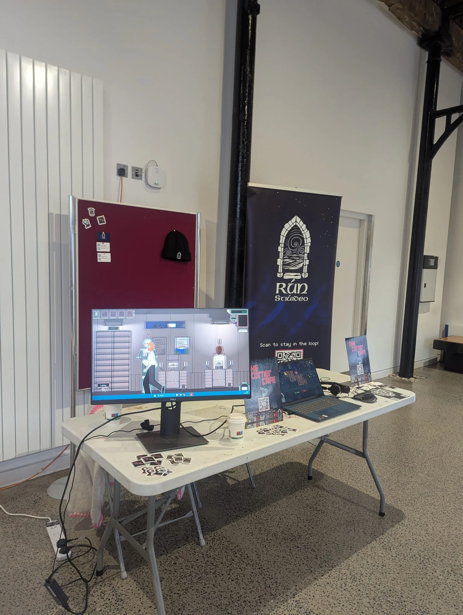 a desk at akumakon showing a cosy pixel art game called The Corner Cafe