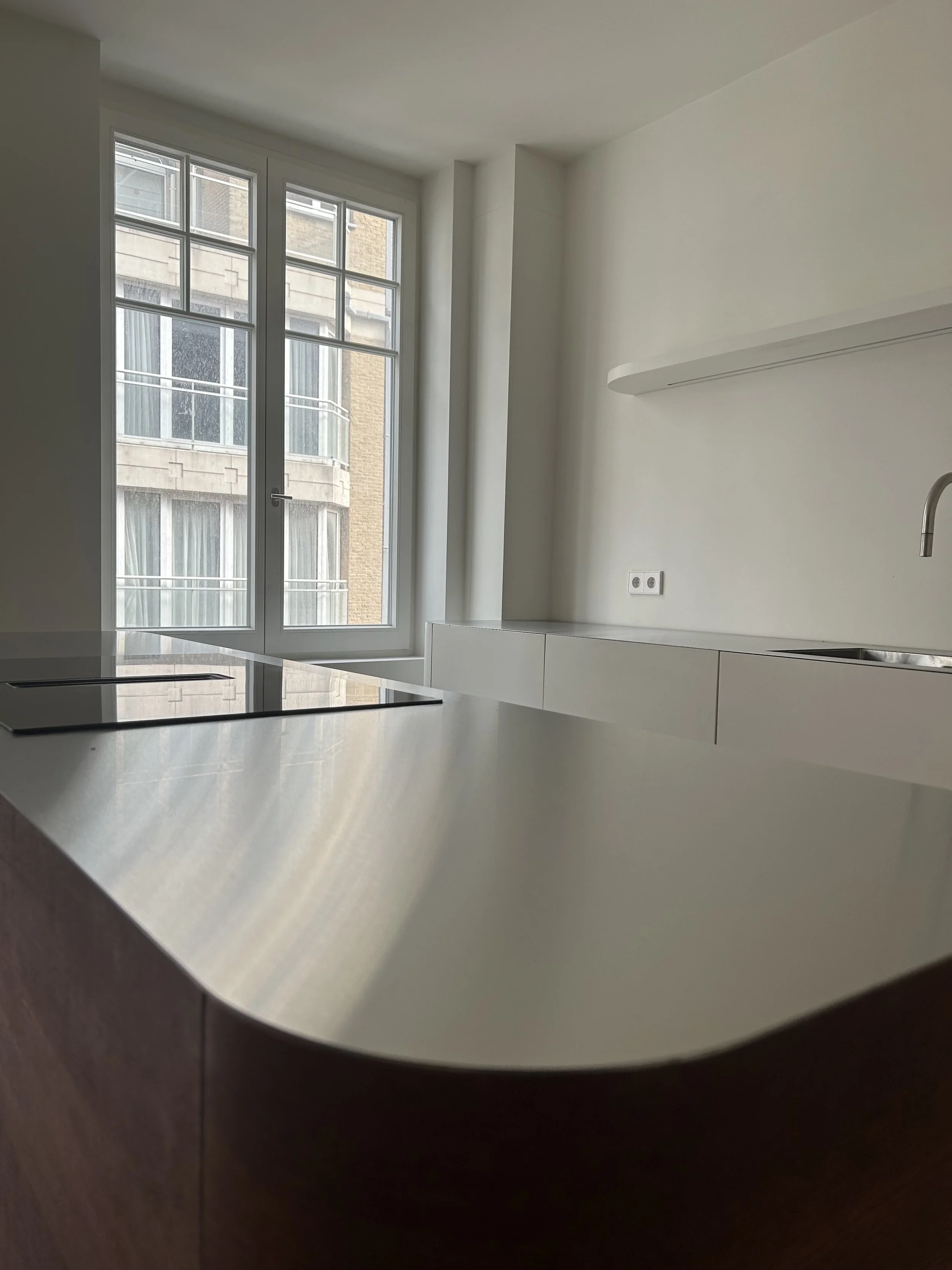 Een wit keukenblad of tafel met een fornuis en een raam in de achtergrond.