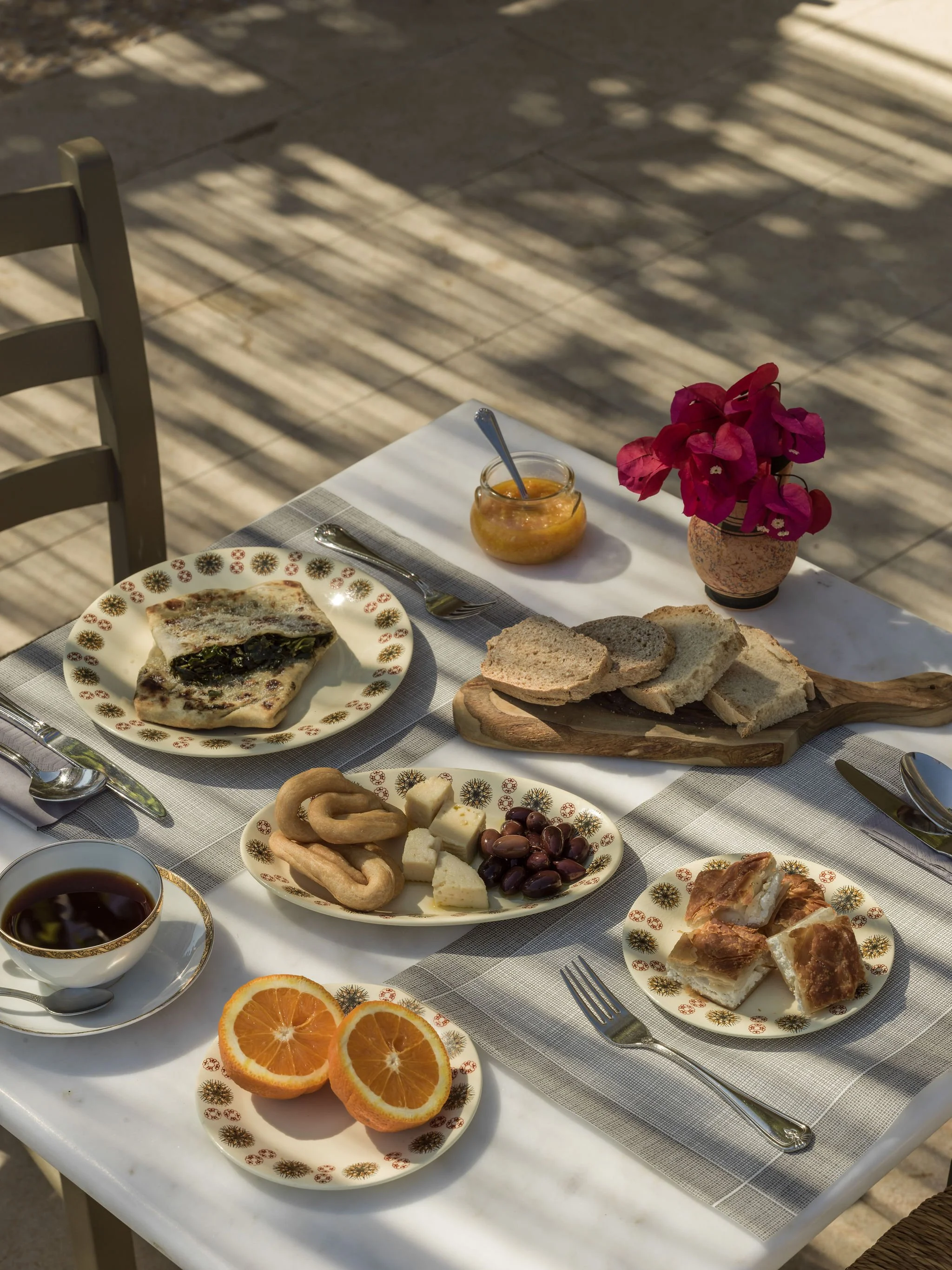 Outdoor barbecue with skewered meat, salads, and drinks on a wooden table, with blurred people and a grill in the background.
