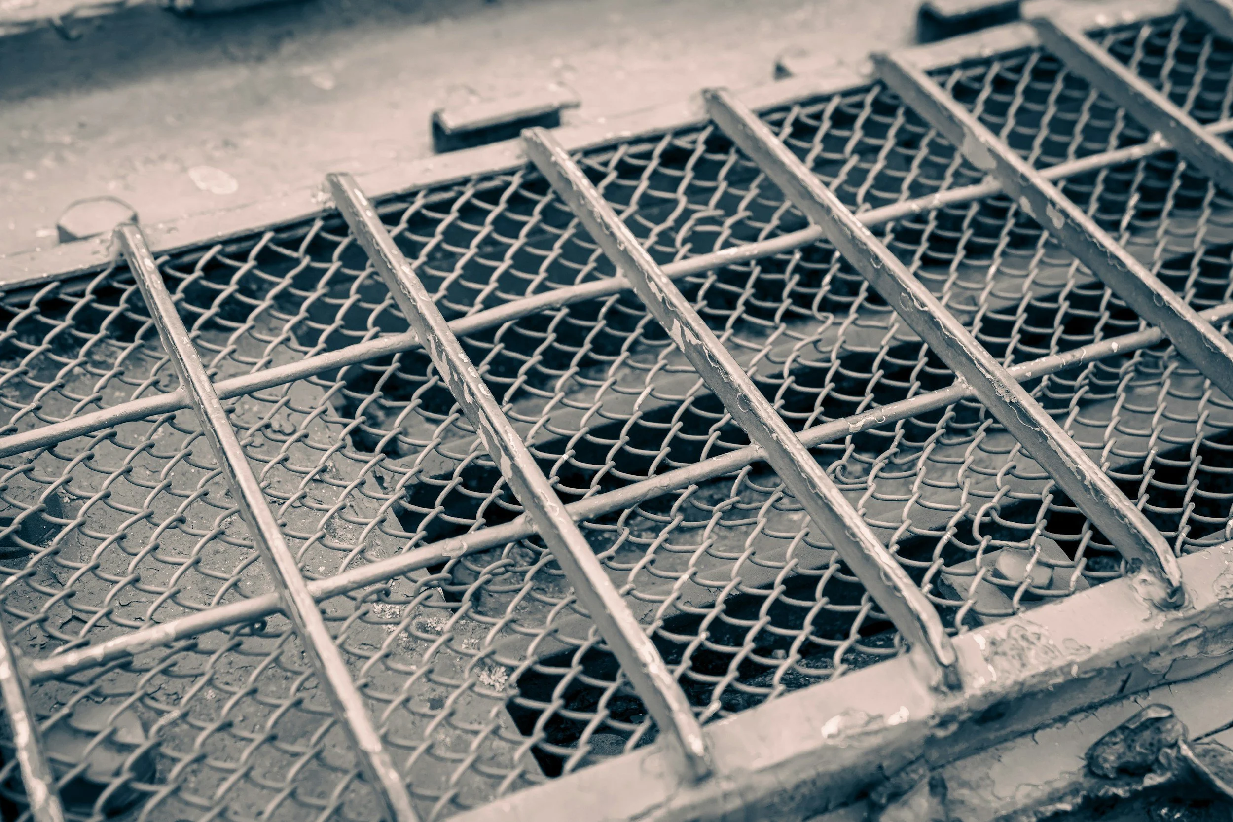 Close-up of a metal drain cover with a grid pattern and peeling paint on its edges, lying on a concrete surface.