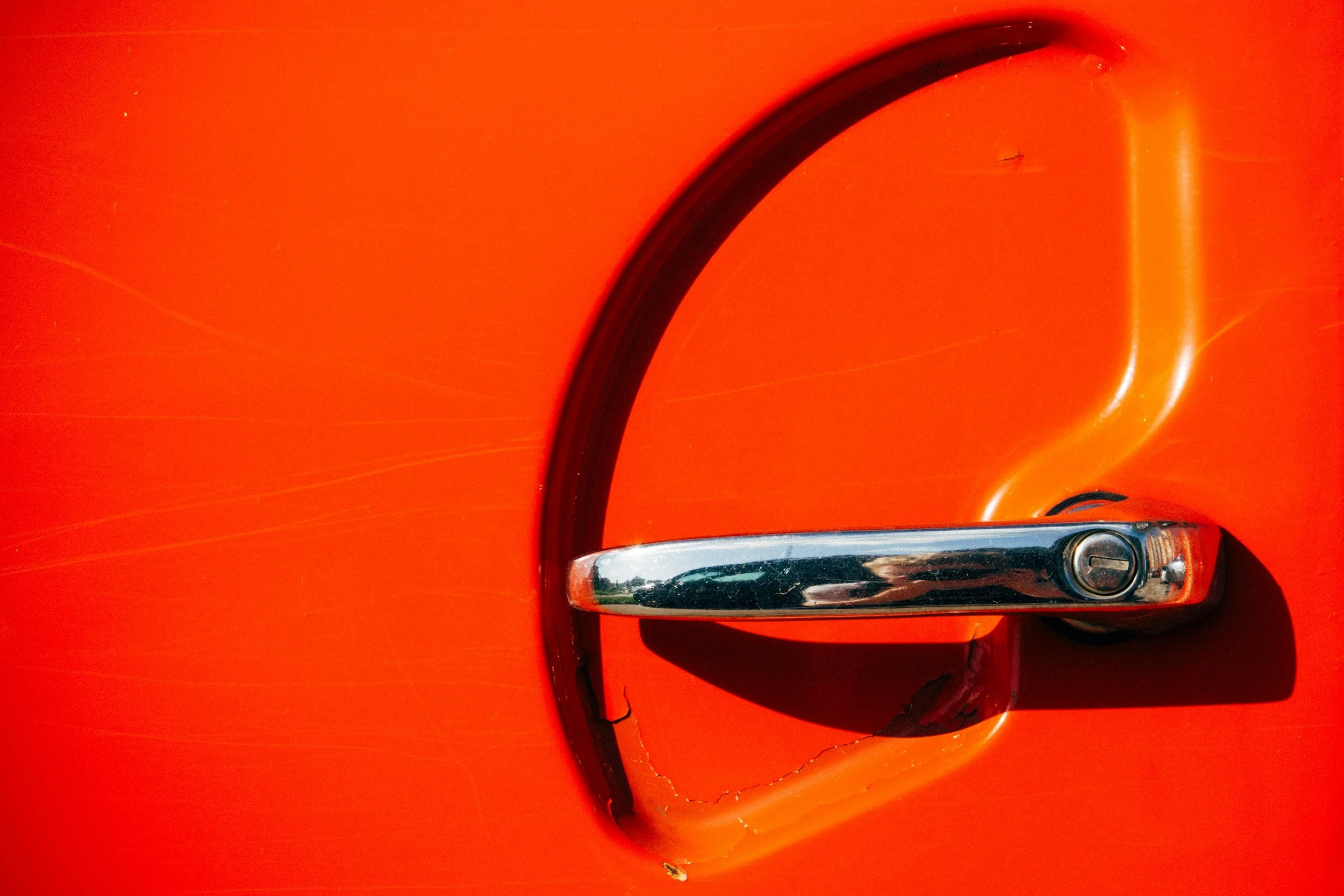 Close-up of a shiny orange car door handle set against the orange painted surface of the car's body.