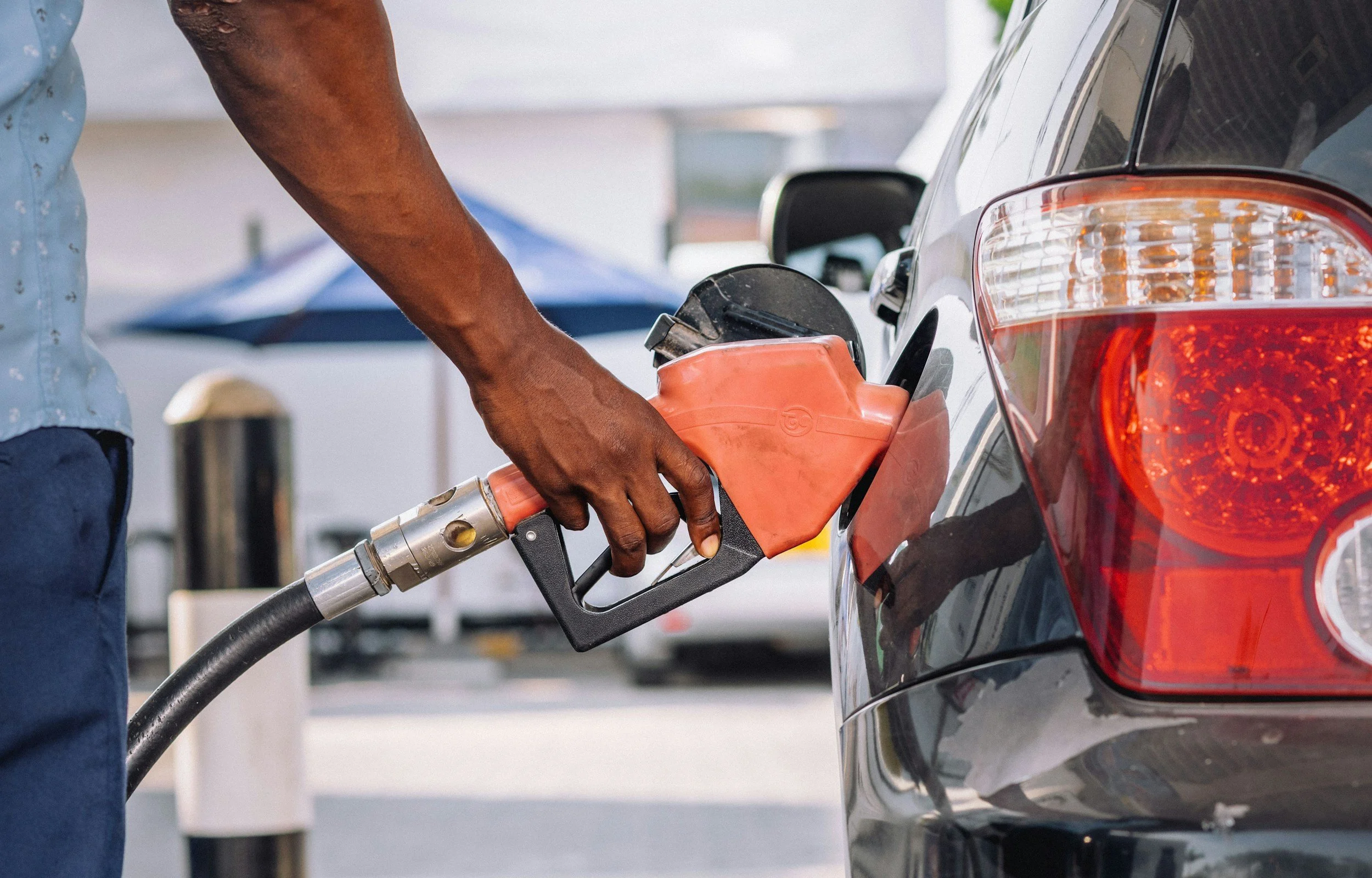 A person holding a fuel pump nozzle filling up a silver car at a gas station.