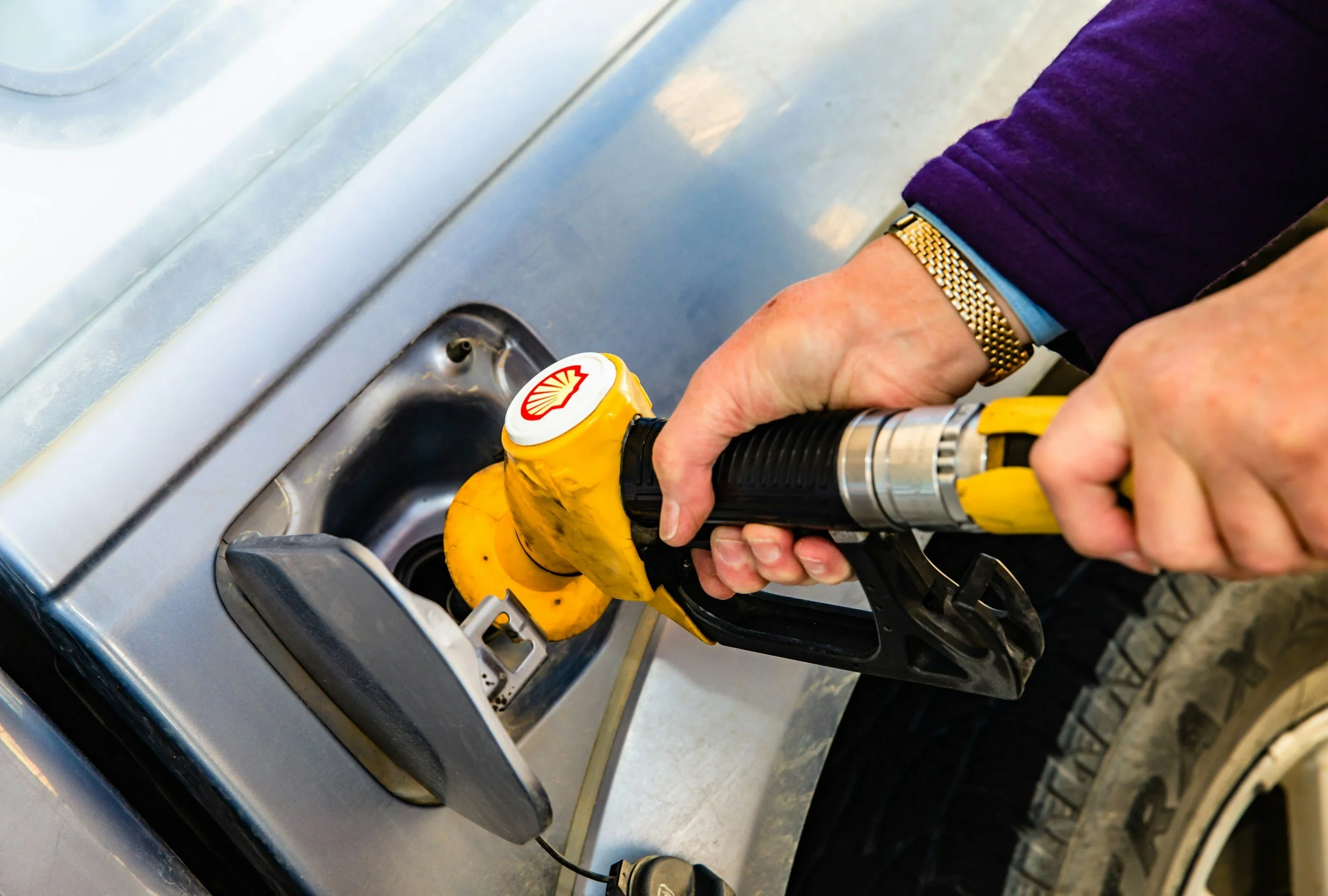 A person wearing a purple jacket and a gold watch is handling a yellow power drill to work on a stove or appliance.