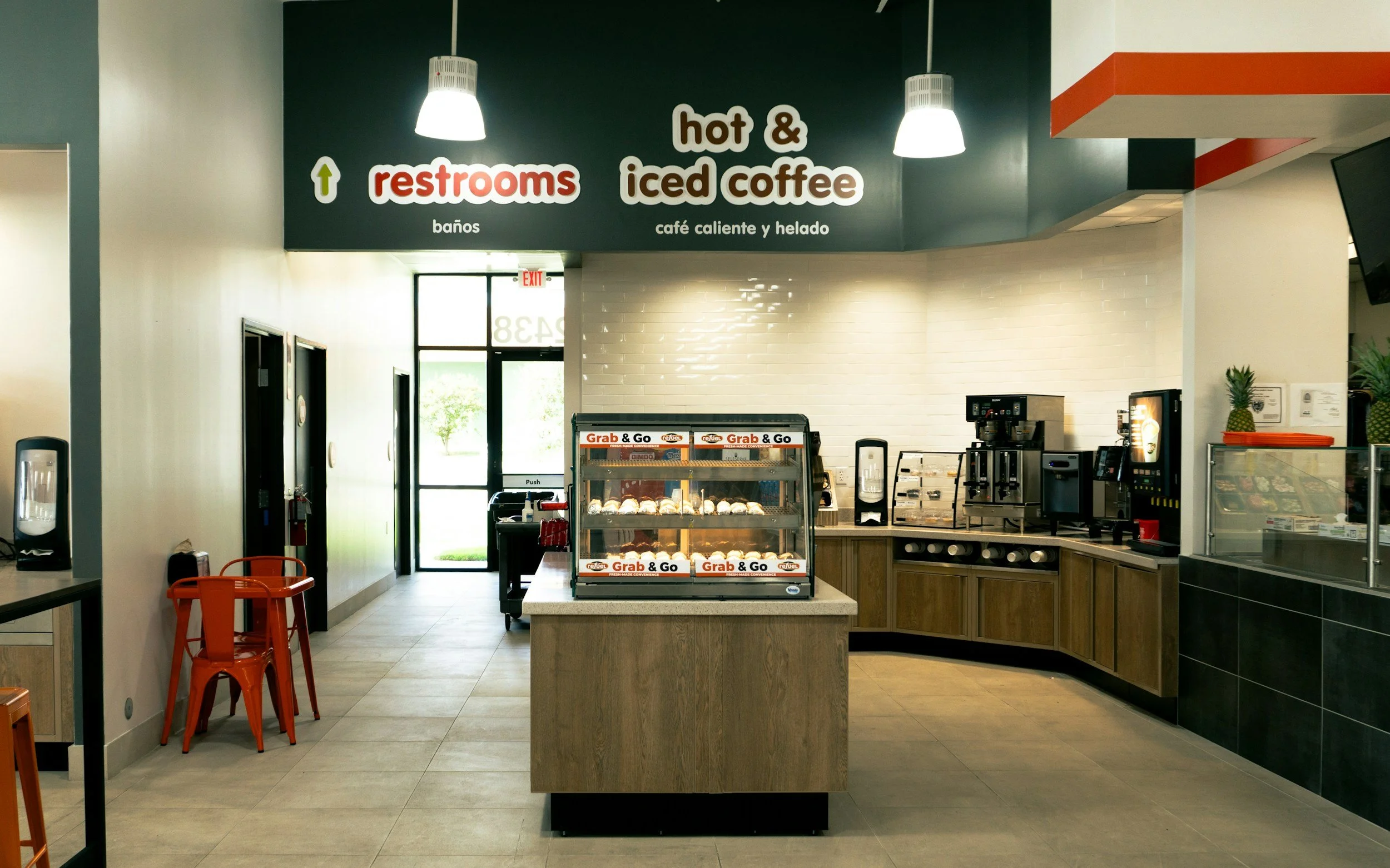 Cafe interior with a central display of Grab & Go baked goods, a coffee station, and a sign indicating restrooms and iced coffee.