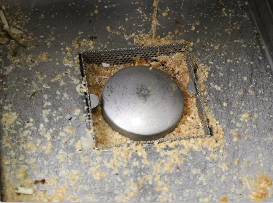 A grease trap cleanout cover with food debris and grease surrounding it.