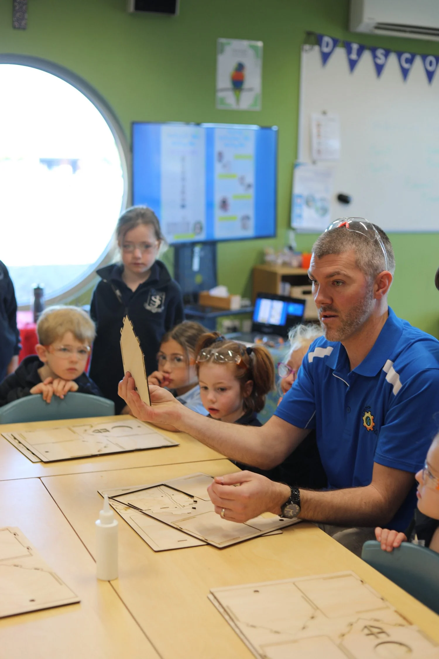 Man teaching a group of children how to assemble wooden puzzles in a classroom.