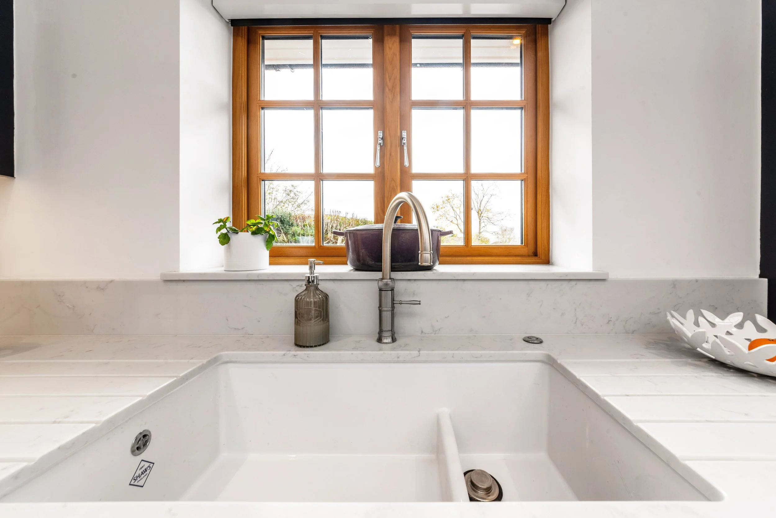 Kitchen sink with a window above it, a potted plant, a soap dispenser, and a decorative bowl on the countertop.