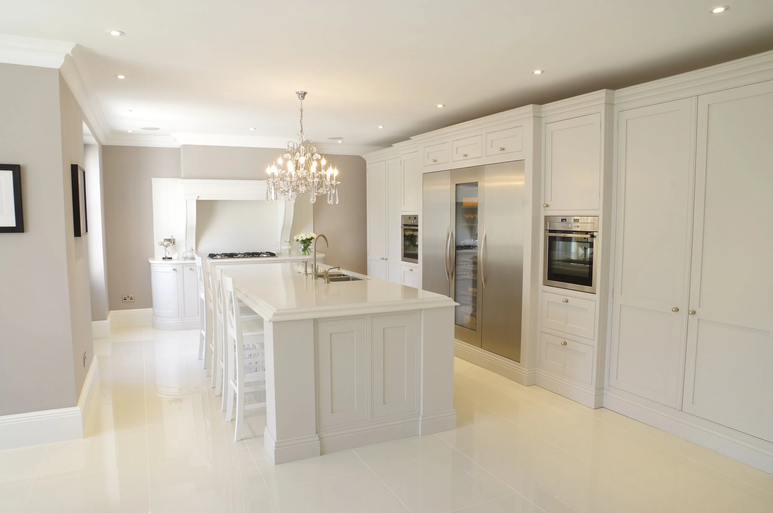 Bright, modern kitchen with white cabinets, stainless steel appliances, a chandelier, and a kitchen island with bar stools.