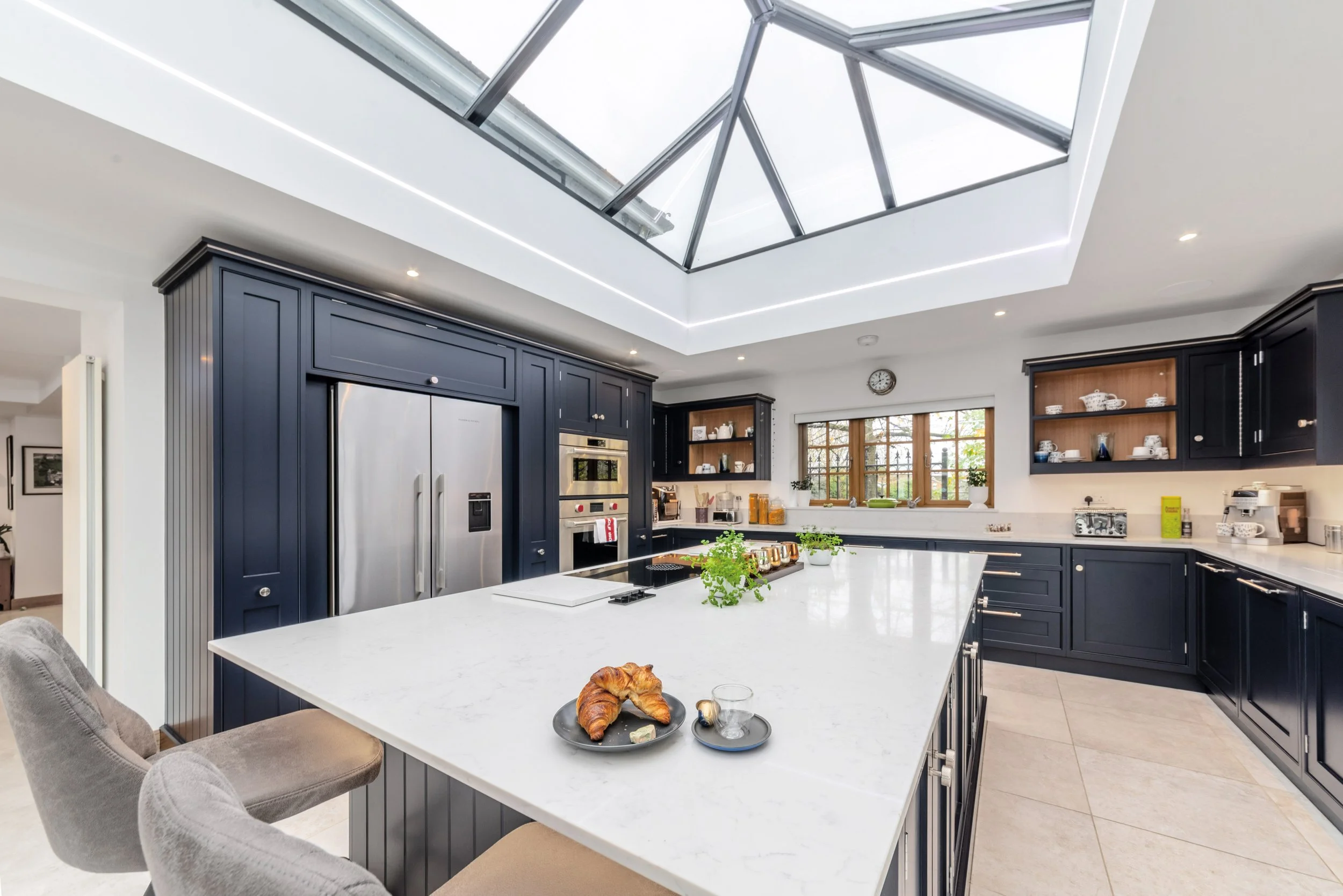 Modern kitchen with navy blue cabinets, white marble island, and large skylight ceiling.