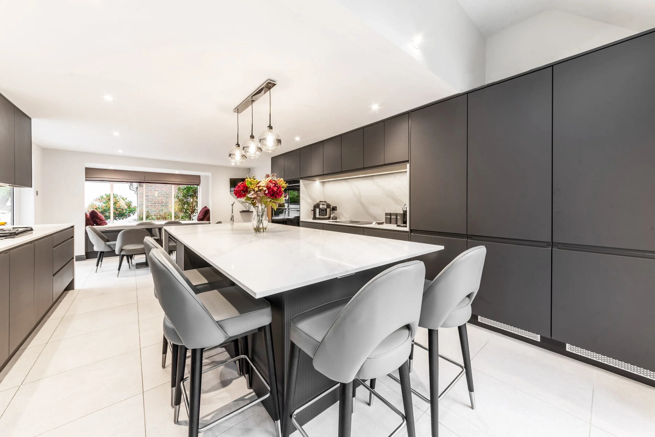Modern kitchen with a large white marble island, gray cabinetry, and a vase of colorful flowers on the island.