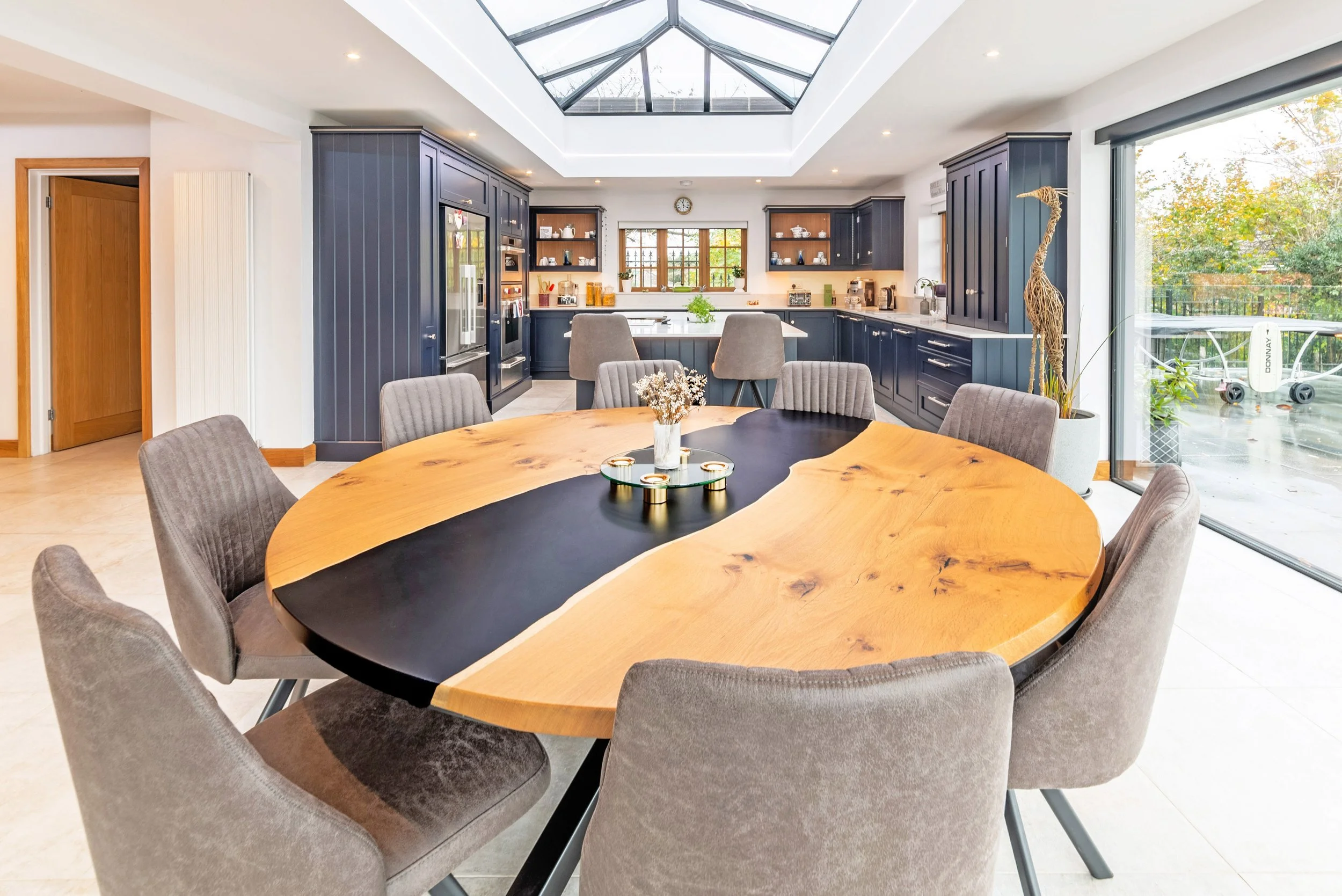 Modern kitchen with dark blue cabinets, a skylight ceiling, a round wooden dining table with grey chairs, and large glass sliding door leading outside.