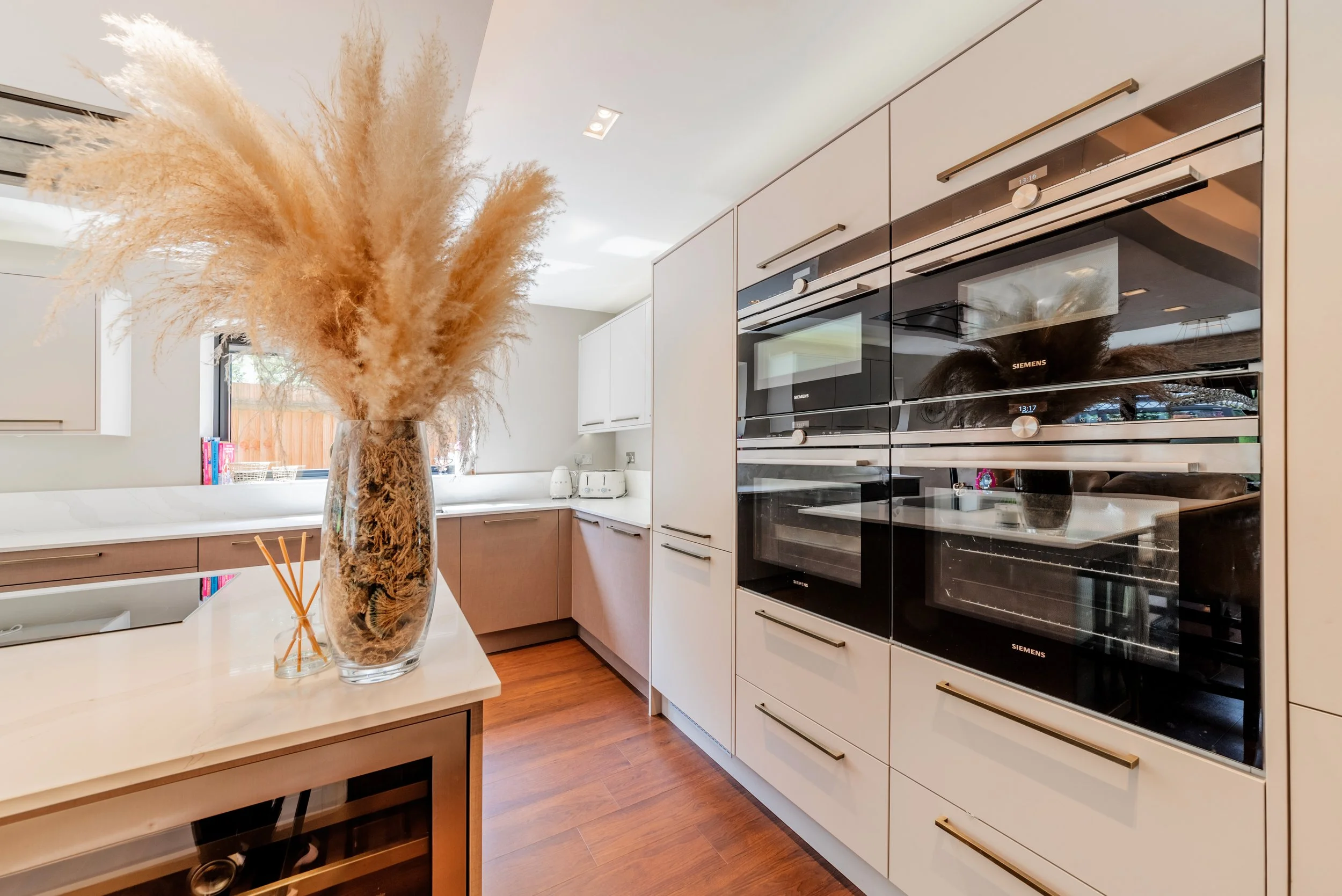 Kitchen with white cabinets, black oven, and large glass vase filled with dried pampas grass on a white countertop.