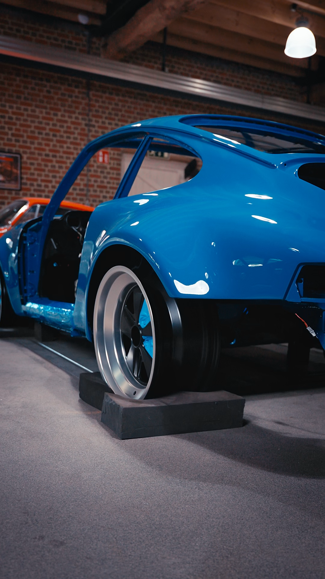 A vintage blue race car displayed indoors, on display stands, with a brick wall background and overhead lighting.