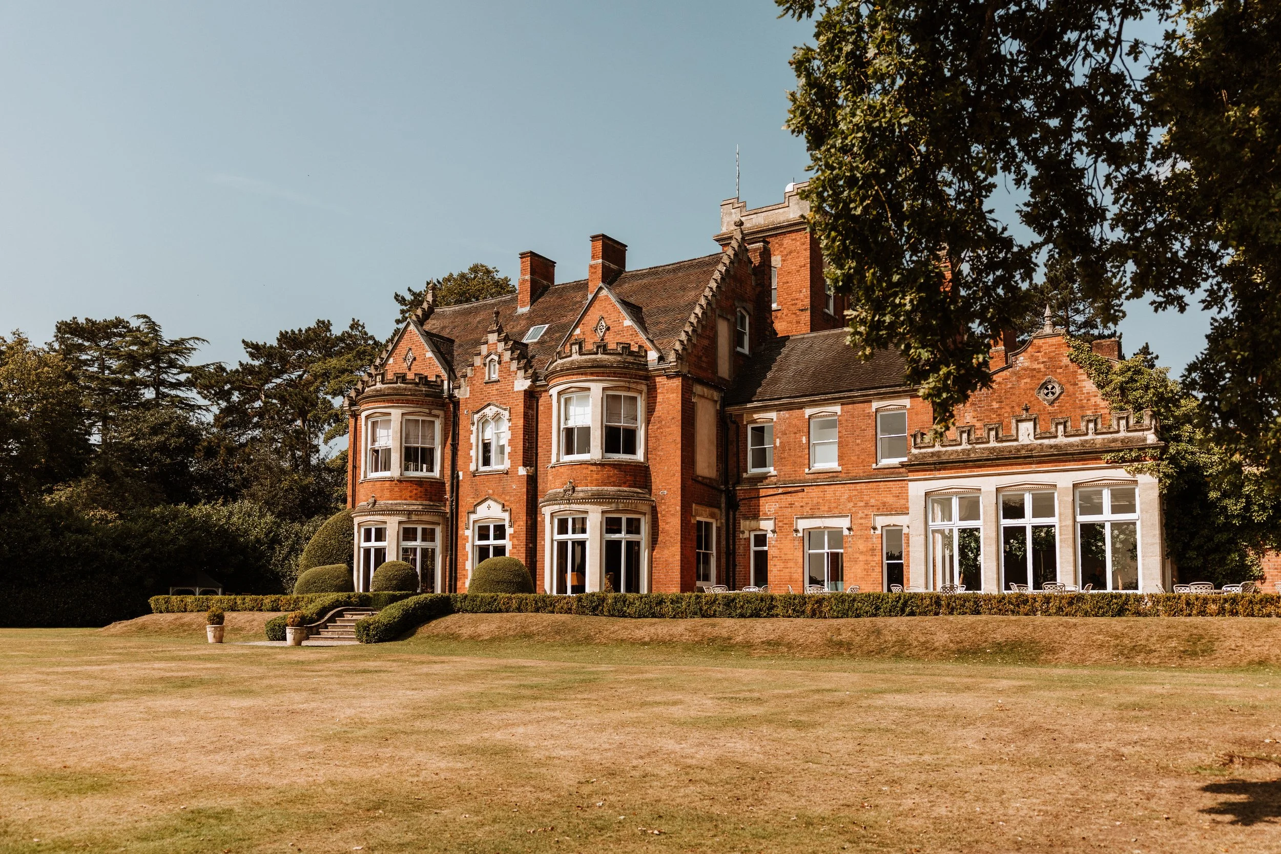 A large, historic red brick mansion with multiple stories, bay windows, and decorative architectural details, surrounded by a well-manicured lawn and trees. Pendrall Hall, Codsall, West Midlands.