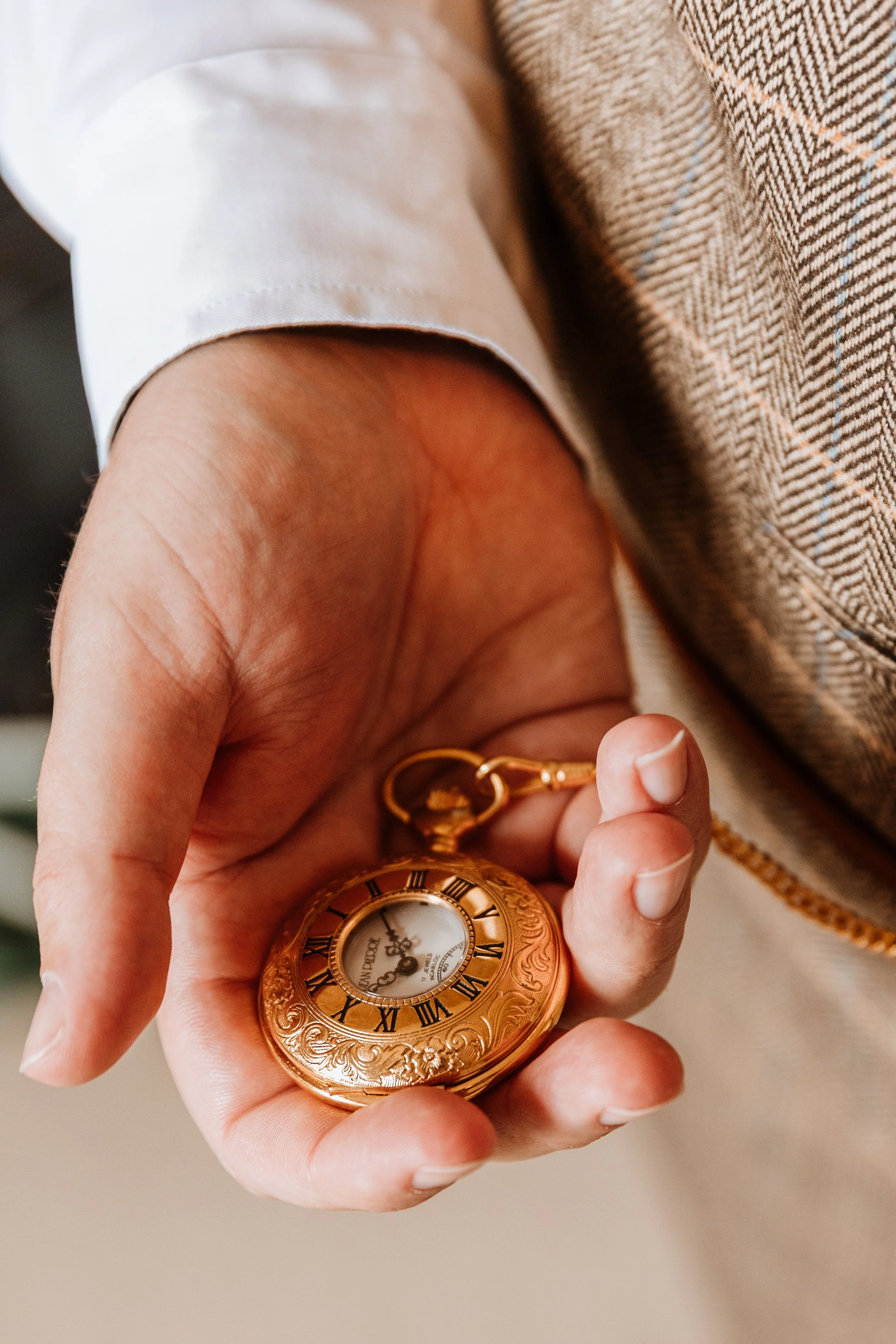 A person holding a vintage gold pocket watch with Roman numerals on the dial.