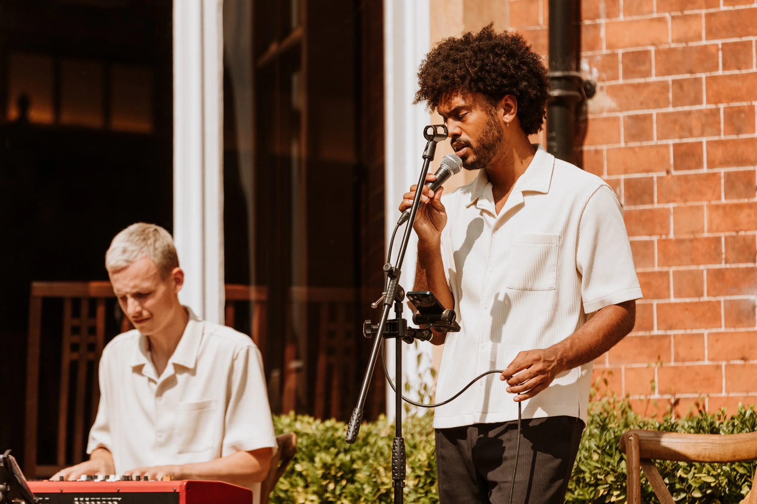 Two men performing music outdoors at night, one singing into a microphone and the other playing a red keyboard.