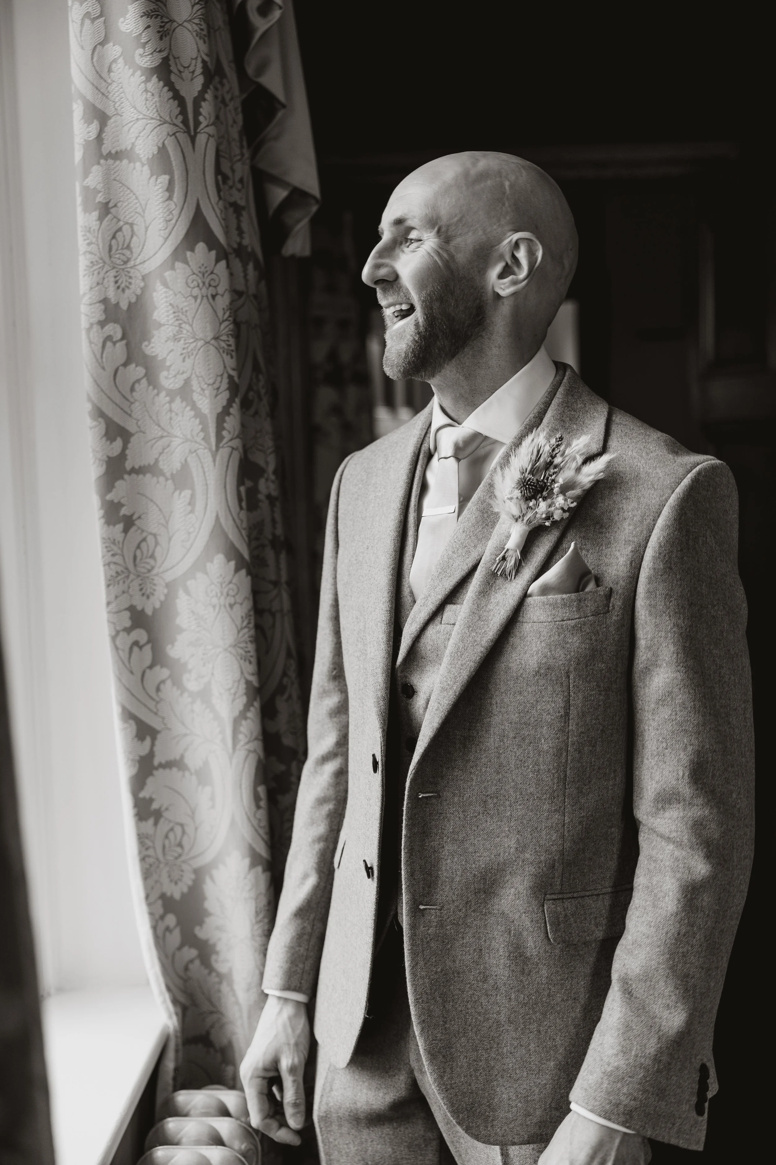 A black and white photo of a smiling man in a suit looking out a window.