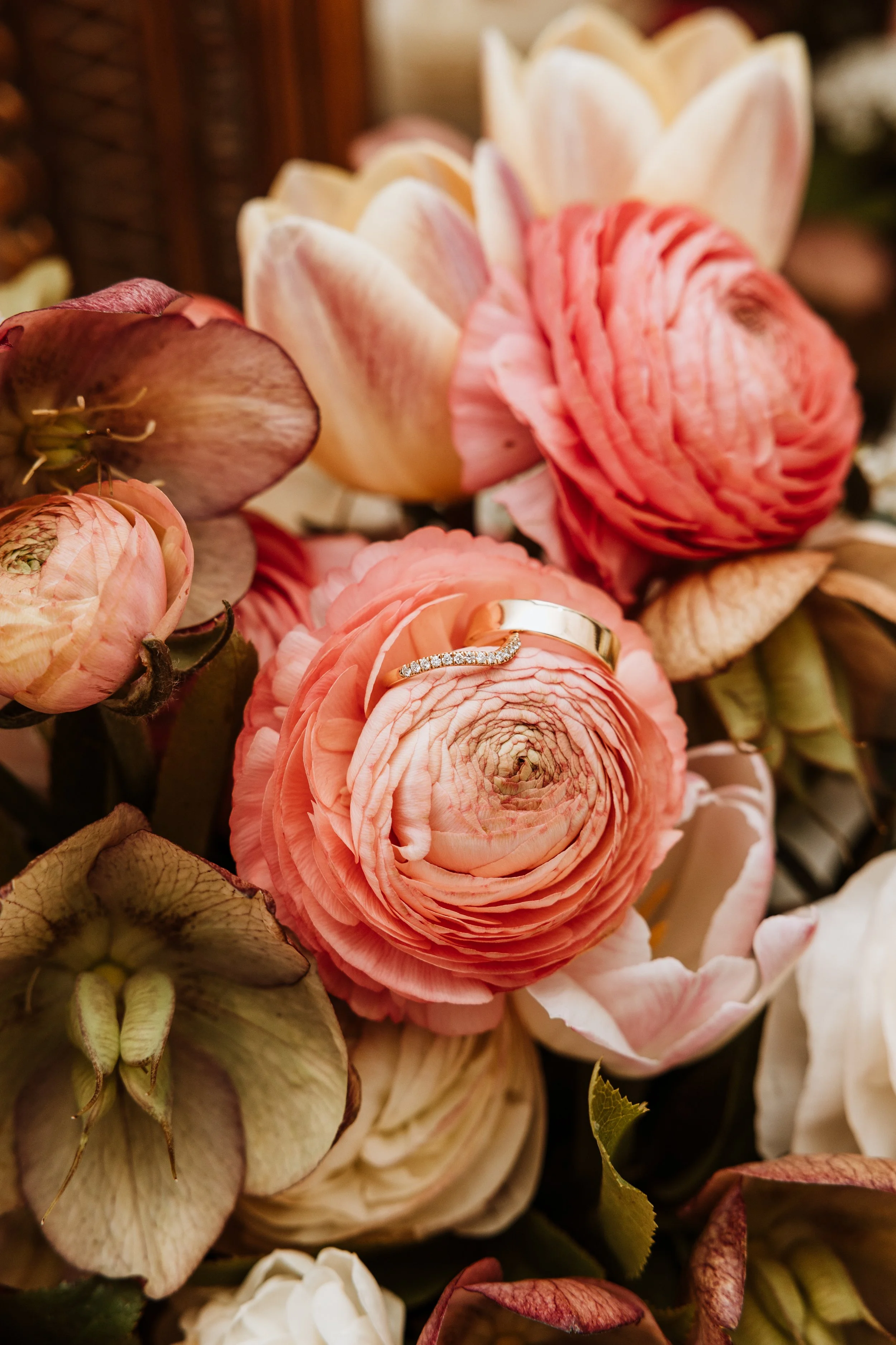 Close-up of pink and cream ranunculus flowers with a silver and diamond ring resting on one of the flowers.