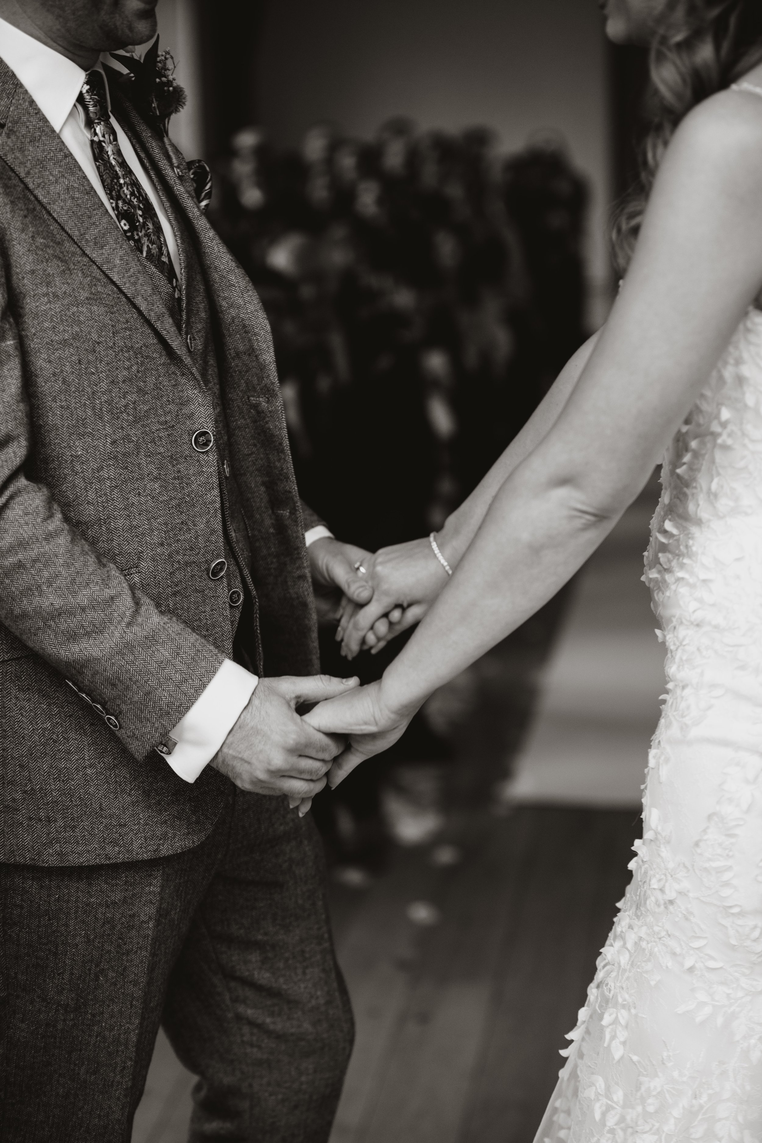 A couple holding hands during a wedding ceremony, with guests in the background.