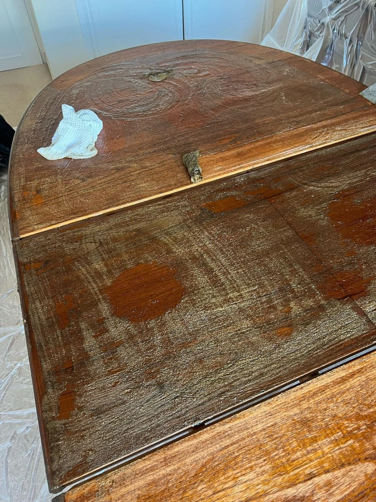 A wooden table with water stains, a piece of wood, a cloth, and some aluminum foil around it.