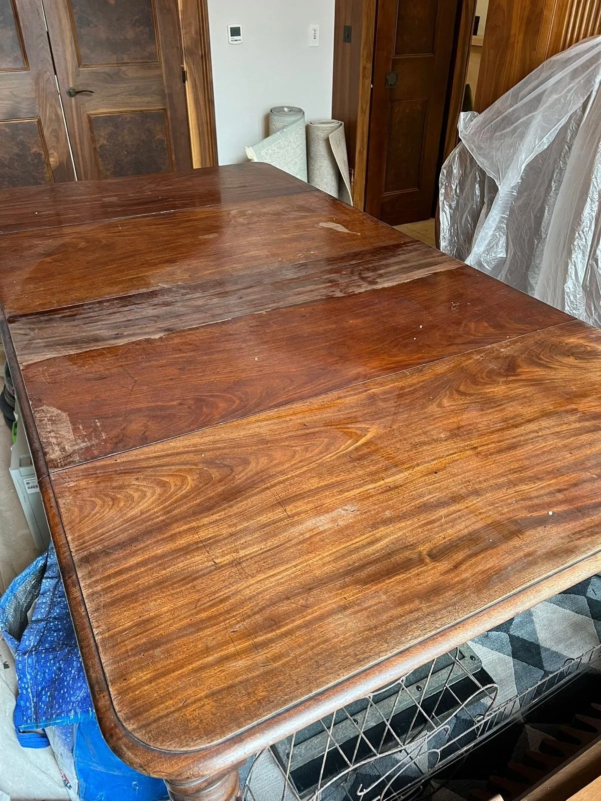 Wooden table with a polished surface in a room with wooden doors and some rolled-up carpets in the background.