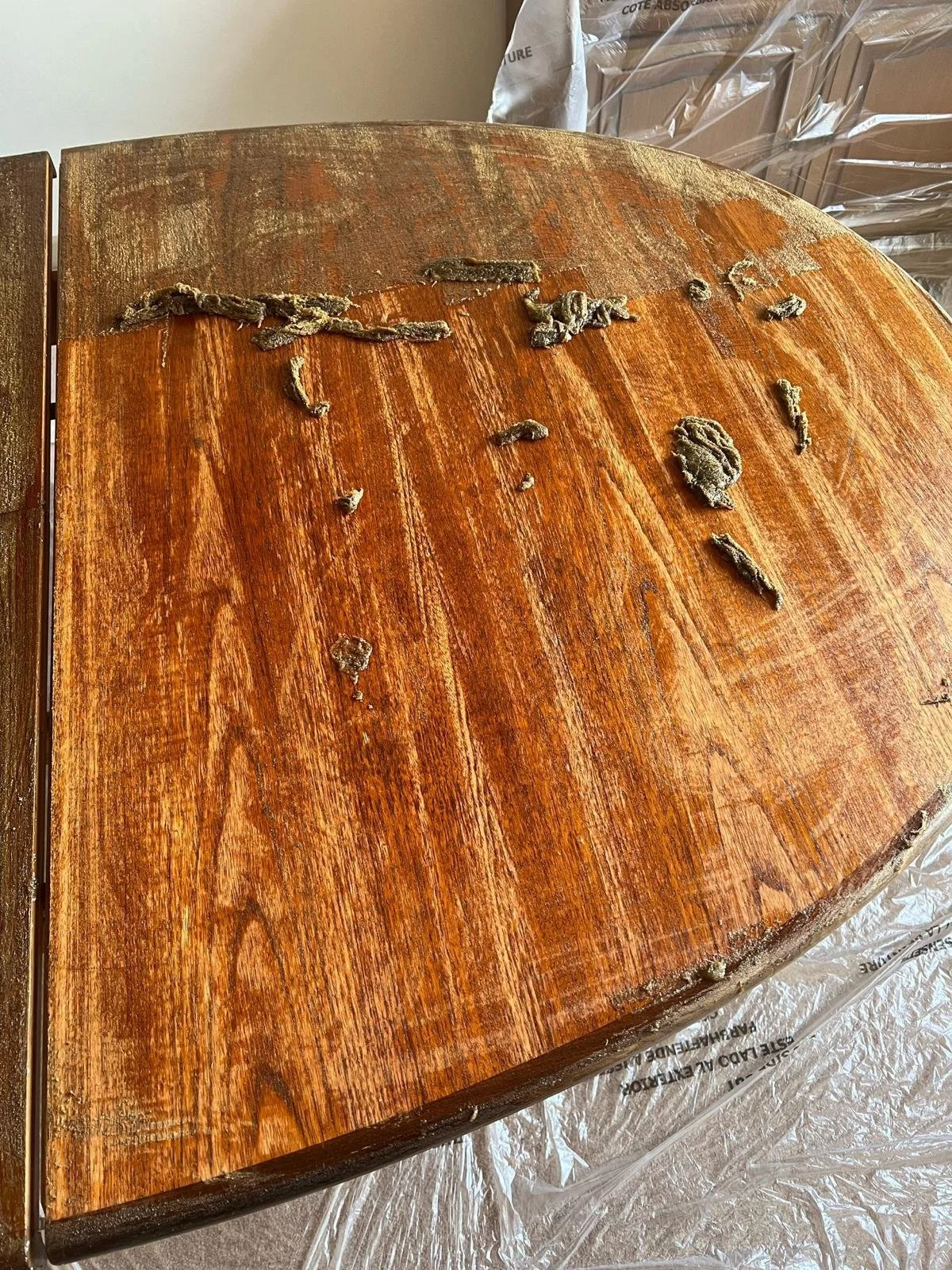 Close-up of a wooden surface with peeling paint and patches of old paint or glue, level surface, surrounded by plastic sheeting and cardboard.