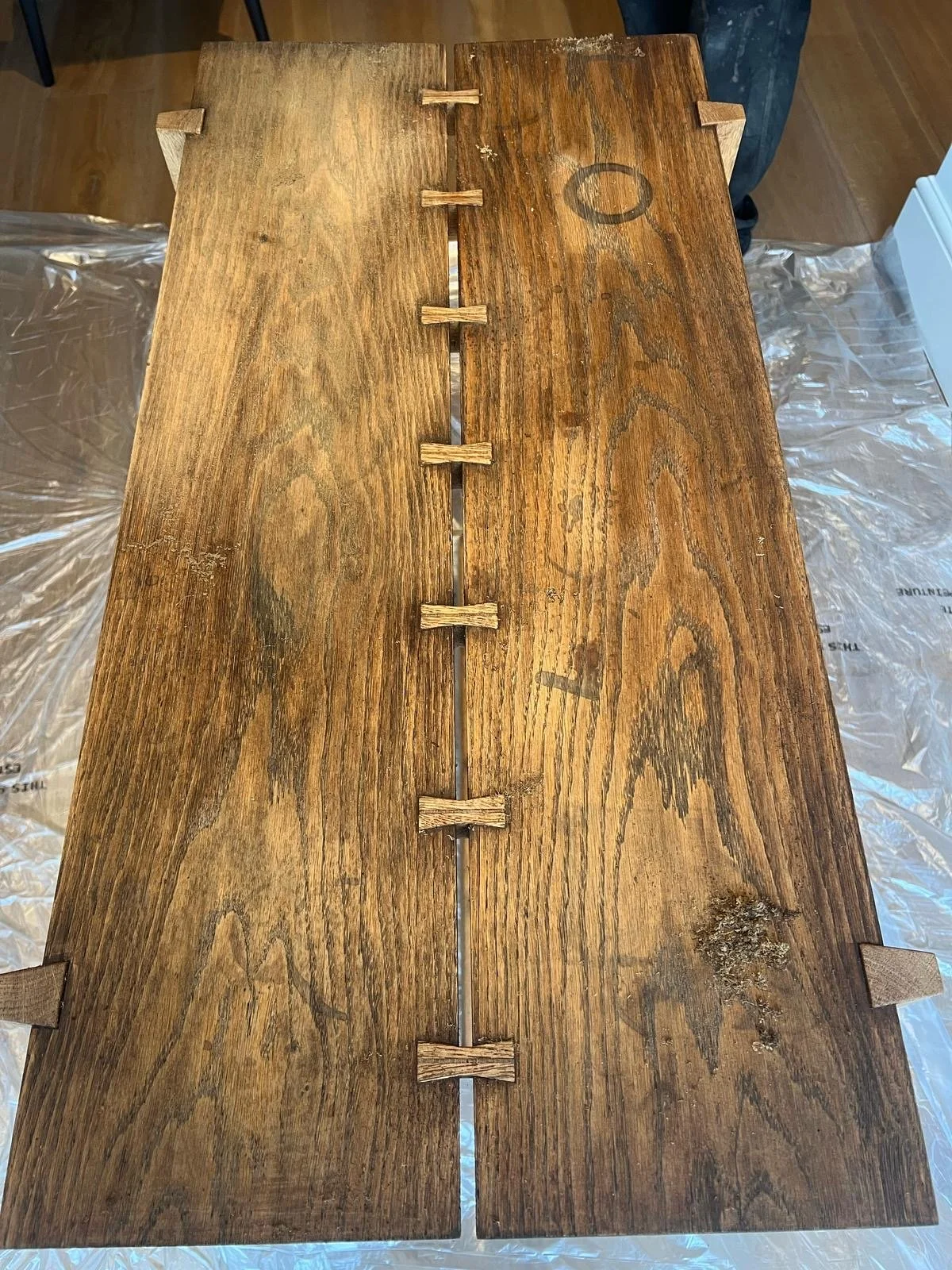 Close-up of a wooden board with a central line of small wooden pieces nailed across the width, showing signs of aging and wear.