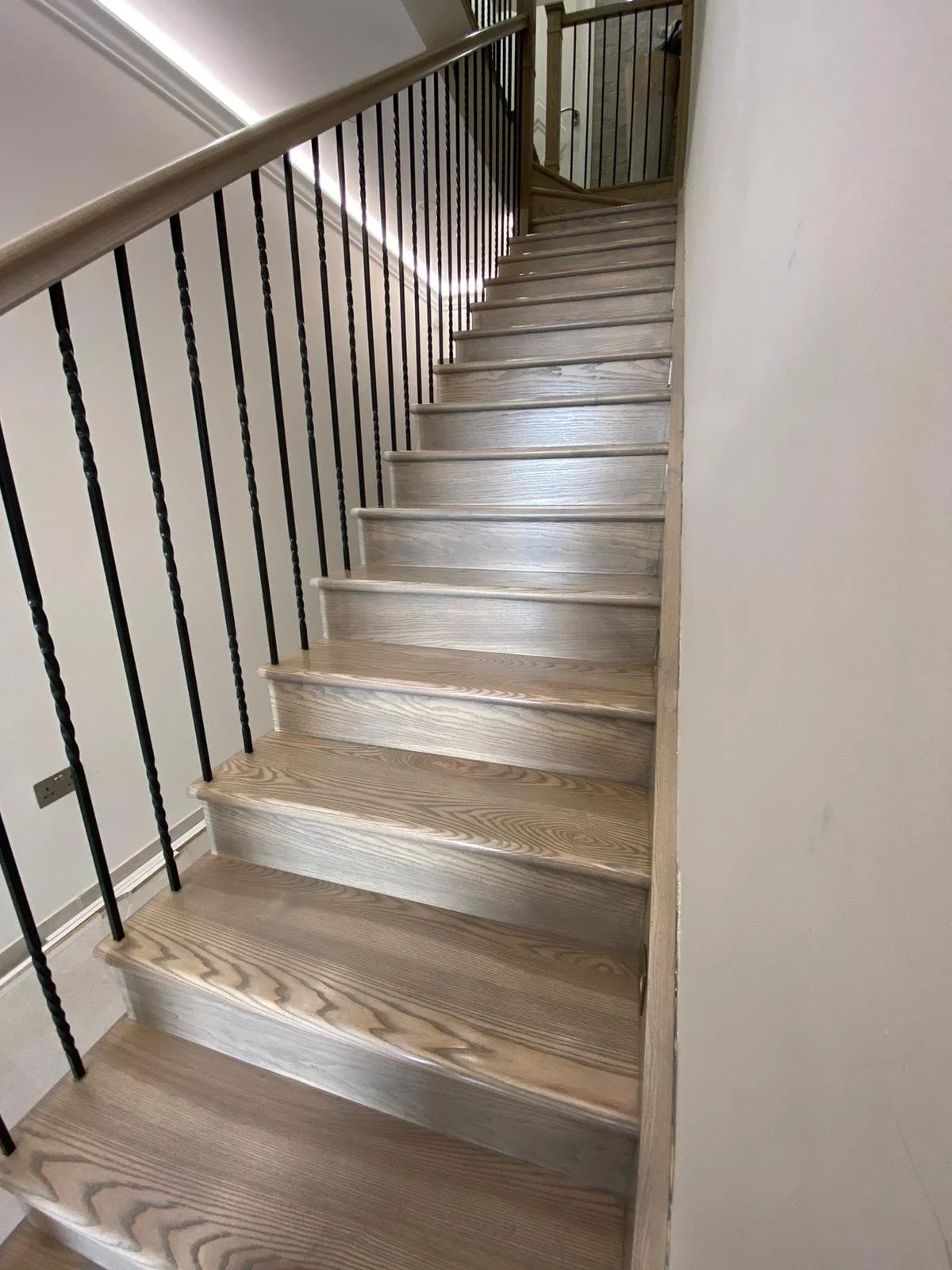 Wooden staircase with black metal balusters and beige handrail in a residential interior.