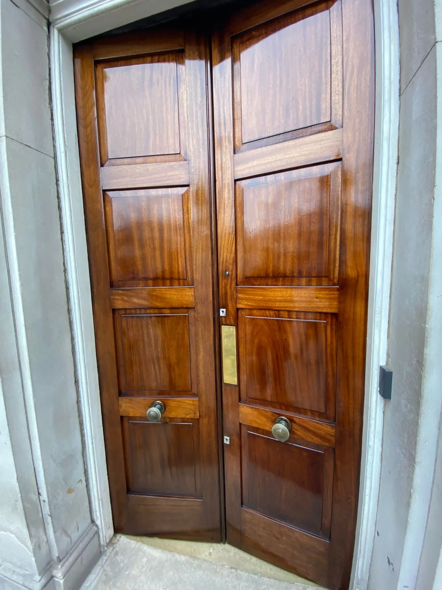 Wooden double door with brass knobs, set in a concrete wall, slightly open.