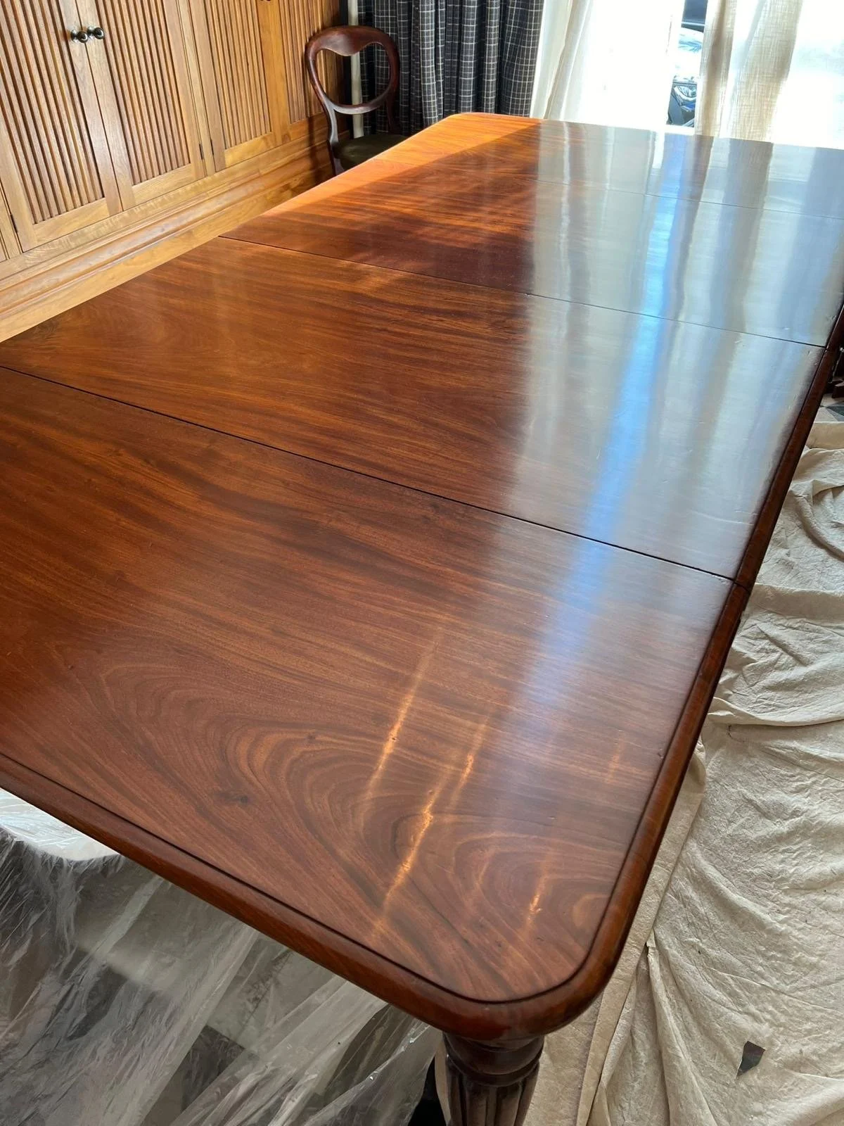 A polished wooden dining table with a glossy finish, overlooking a room with a window and curtains.