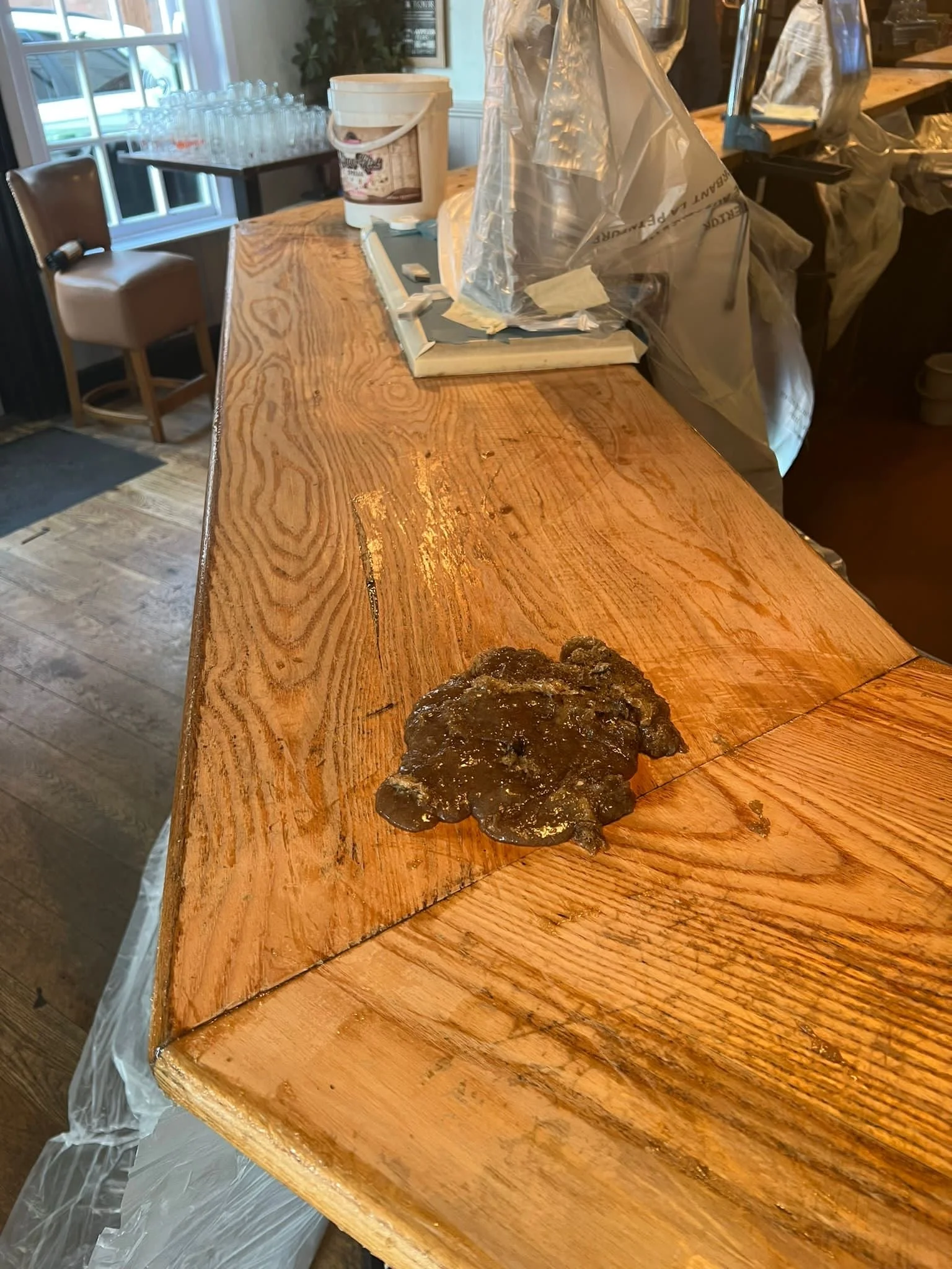 A wet, dark, irregular-shaped substance on a wooden countertop in a restaurant or cafe setting.