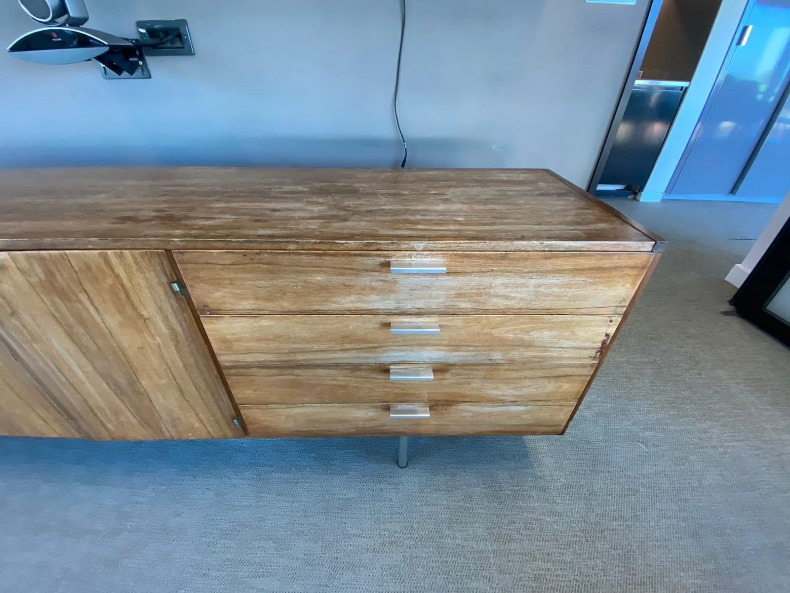 A wooden cabinet with four drawers and metallic handles, positioned against a plain wall.
