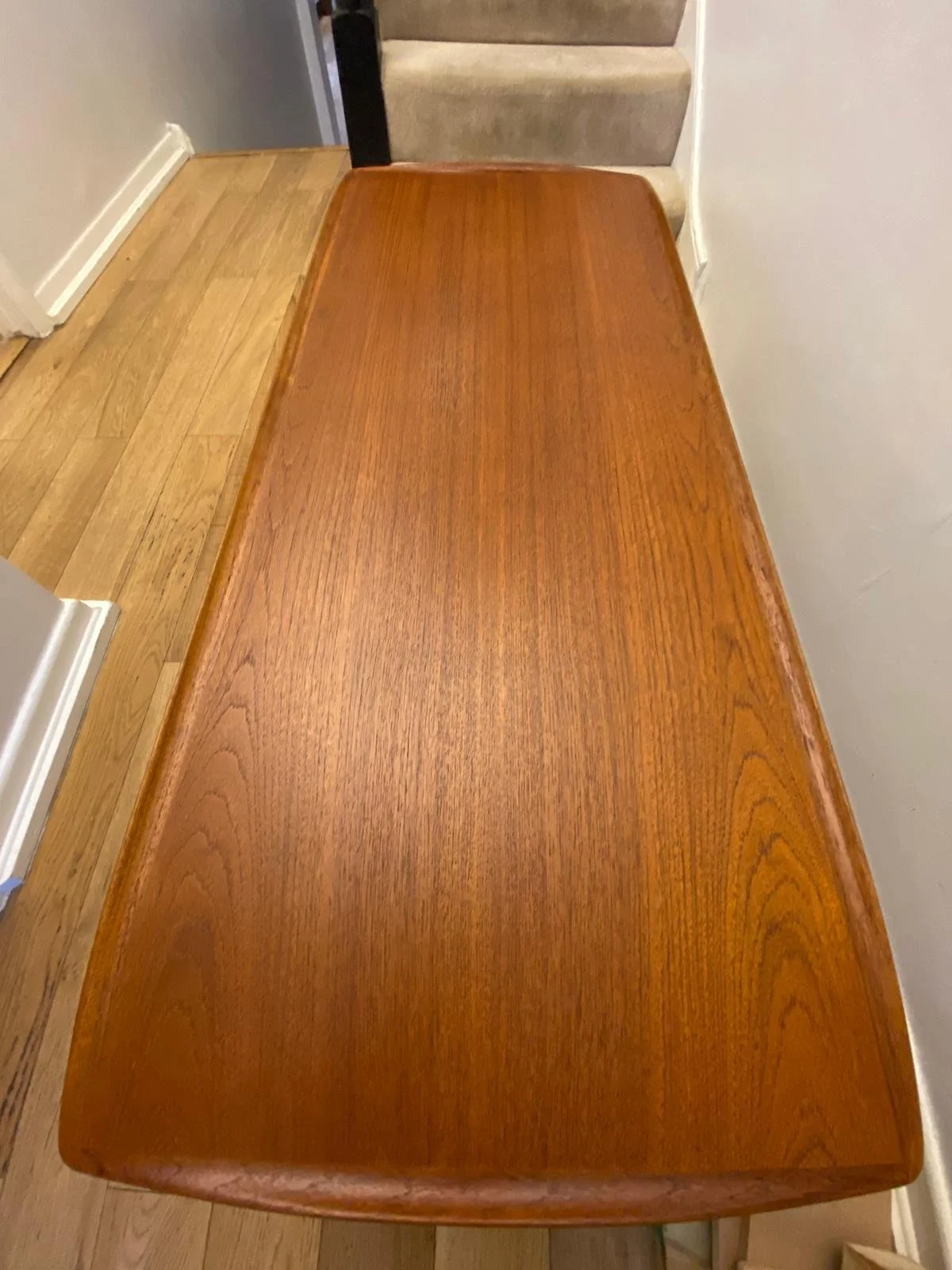 A long wooden dining table with a polished surface in a room with hardwood floors and a staircase in the background.
