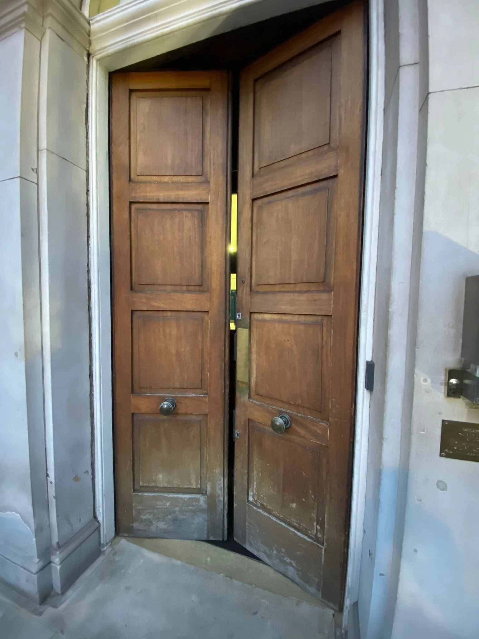 Wooden double doors with knobs, slightly open, inside a building with stone walls.